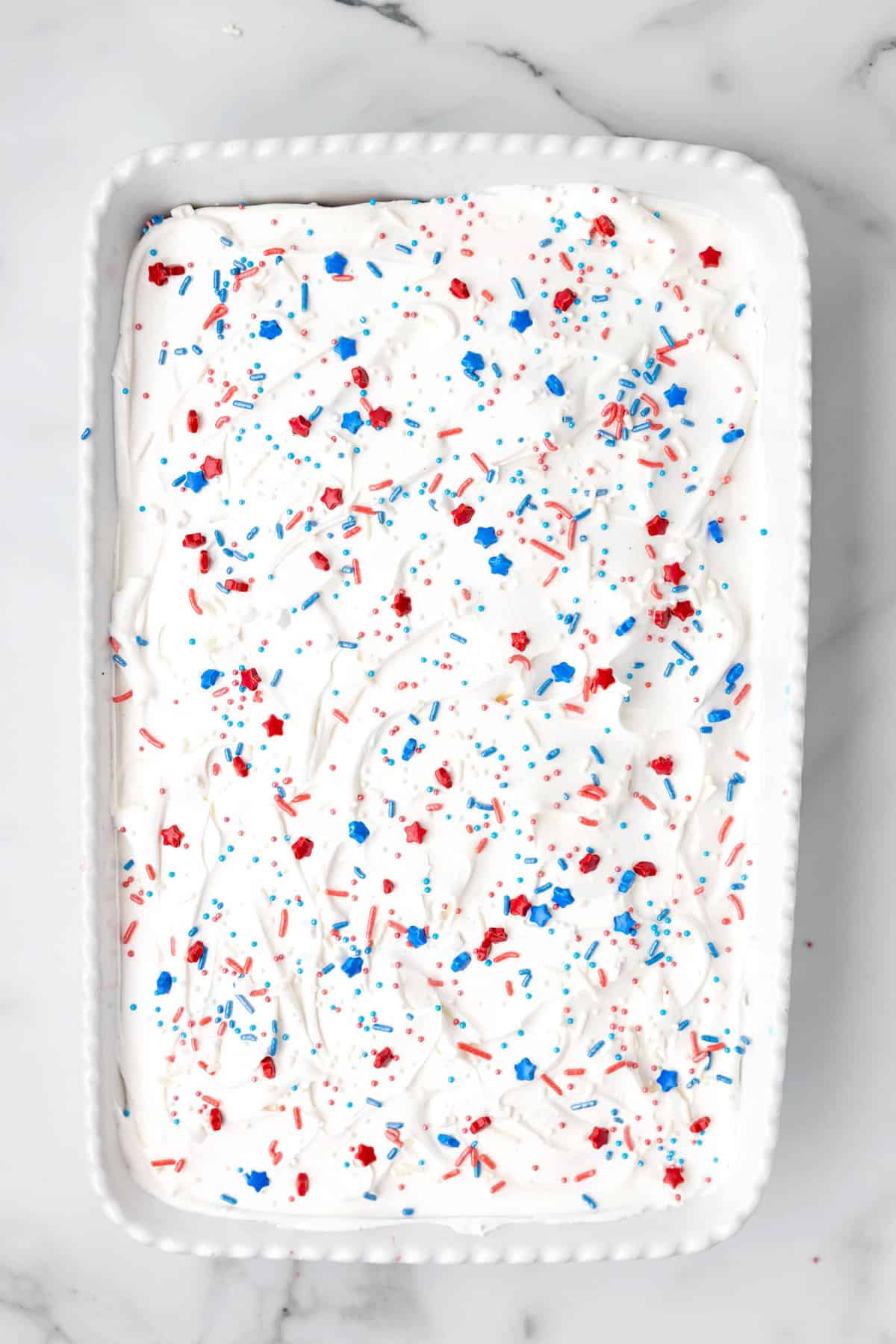 Adding patriotic sprinkles to frosting for Red White Blue Poke Cake