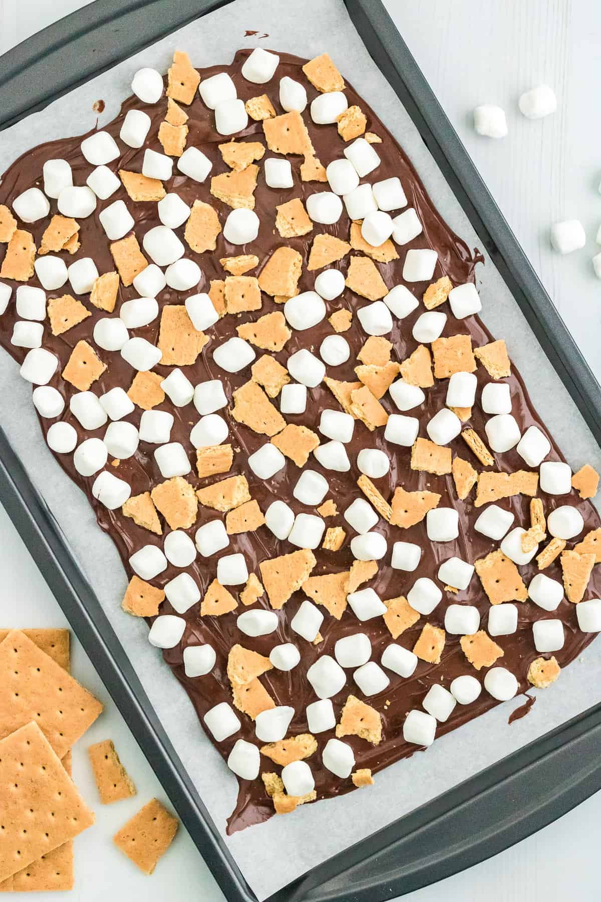 Spread the Chocolate flat on a piece of parchment paper in a cookie sheet & add the broken graham crackers and marshmallows on top.