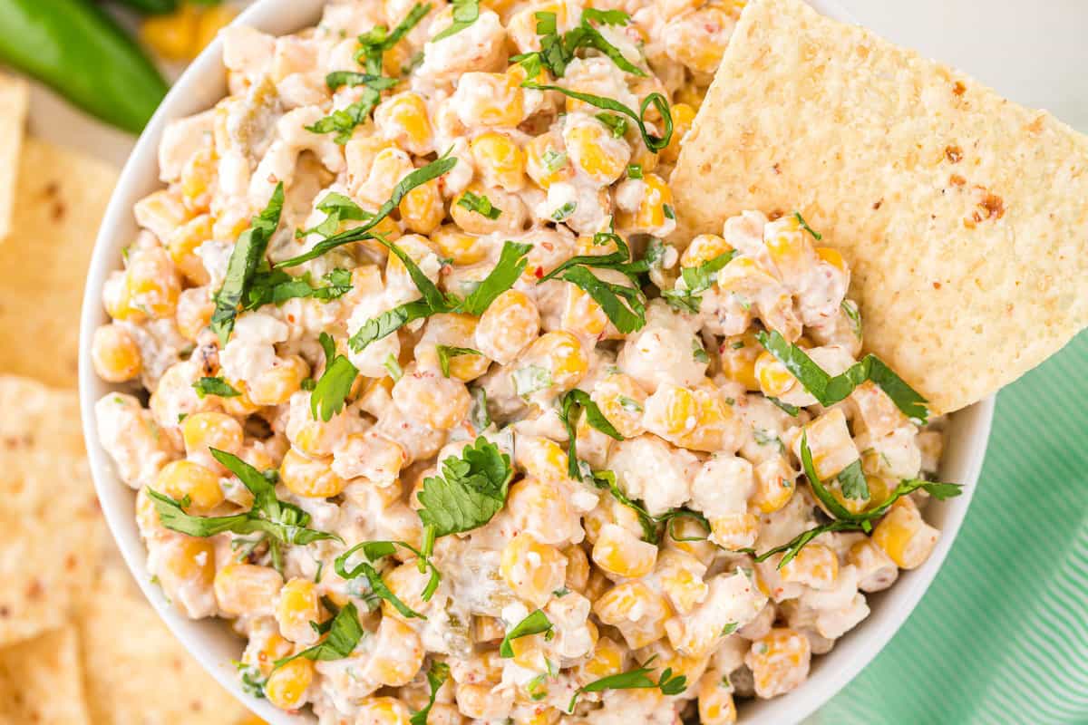 This is a crowd pleaser Mexican Corn Dip Recipe in a bowl with a tortilla chip