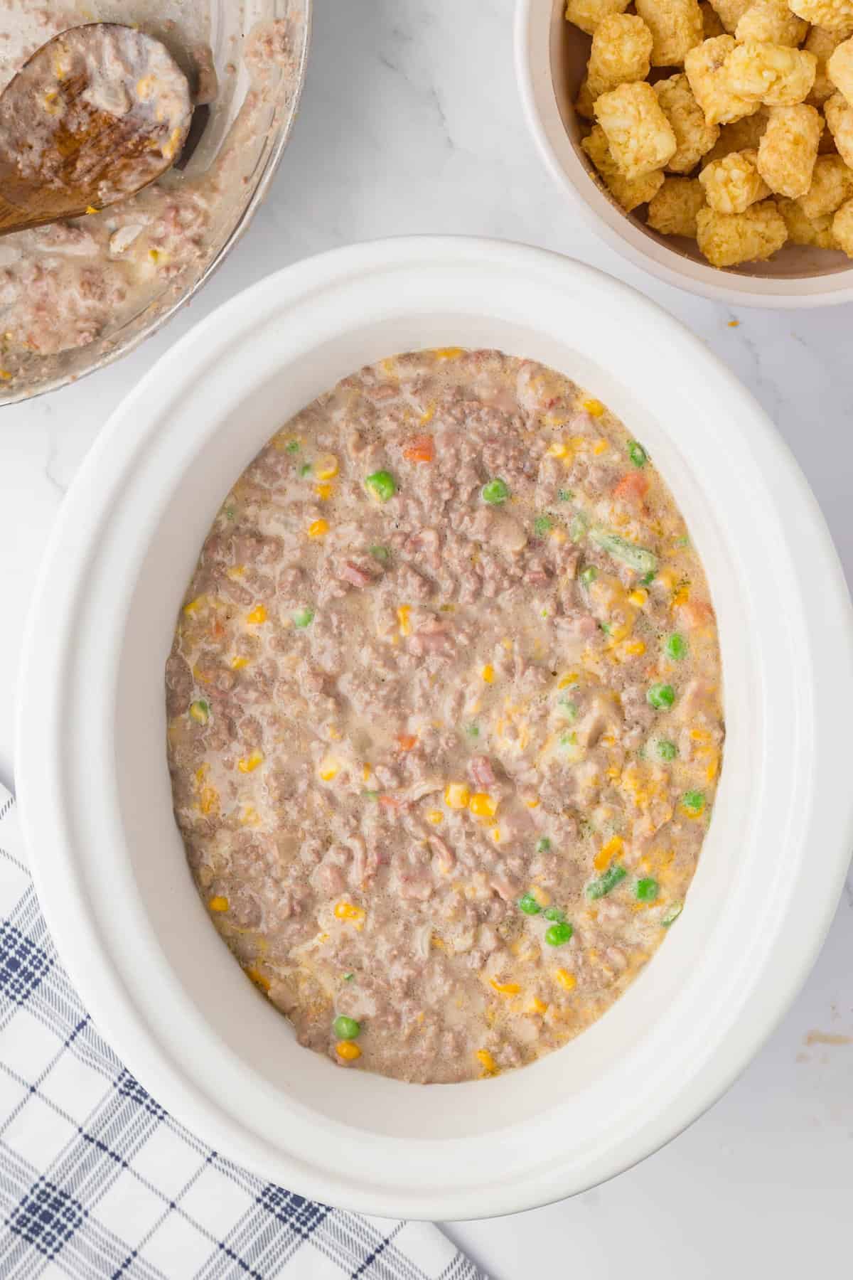 Covering tator tot layer with blended meat mixture for Bacon Cheeseburger Crock Pot Tater Tot Casserole