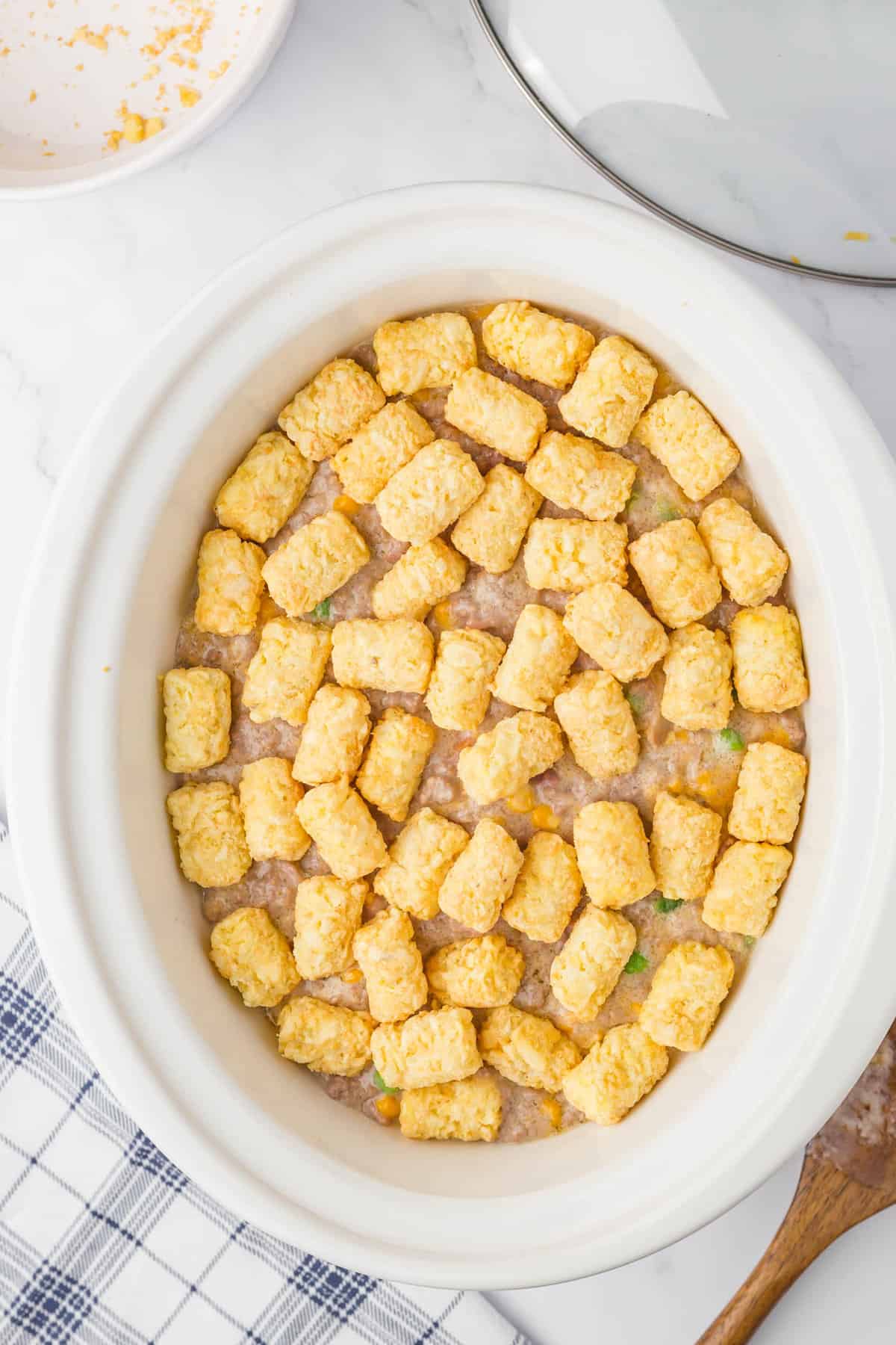 Topping meat mixture with tator tots in crock pot for Bacon Cheeseburger Crock Pot Tater Tot Casserole