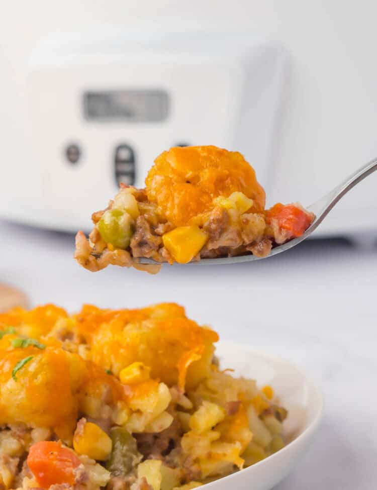 Crock Pot Tater Tot Casserole Recipe on Plate with a Forkful Ready to Enjoy with Crock Pot in Background