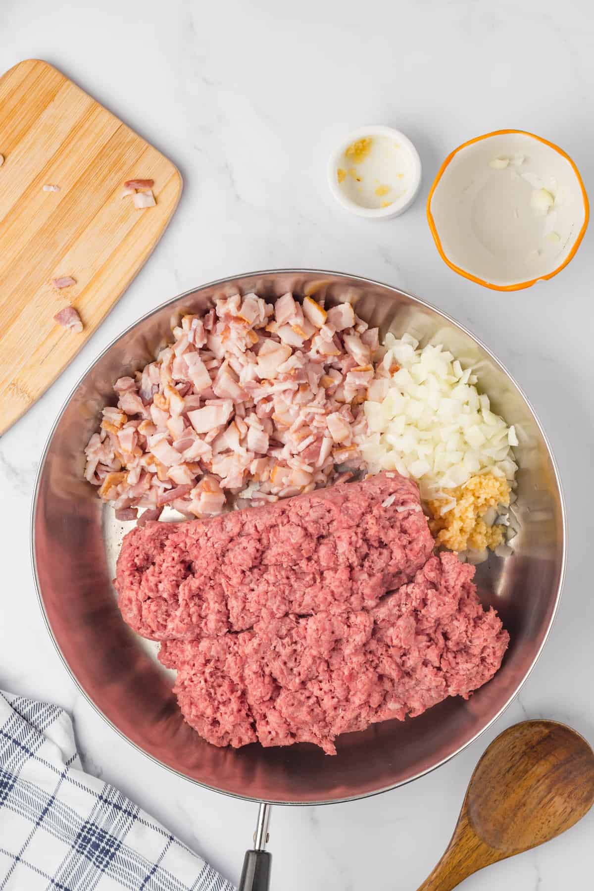 Adding onion and garlic to ground beef and chopped bacon in stovetop skillet ready to brown for Bacon Cheeseburger Crock Pot Tater Tot Casserole