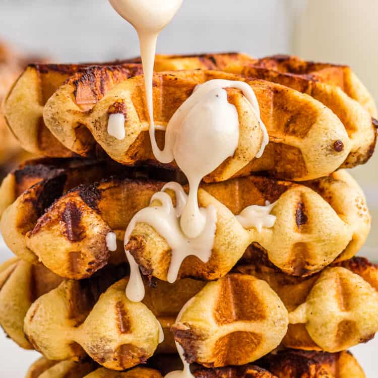 Cinnamon Roll Waffles stacked on plate with drizzle of frosting