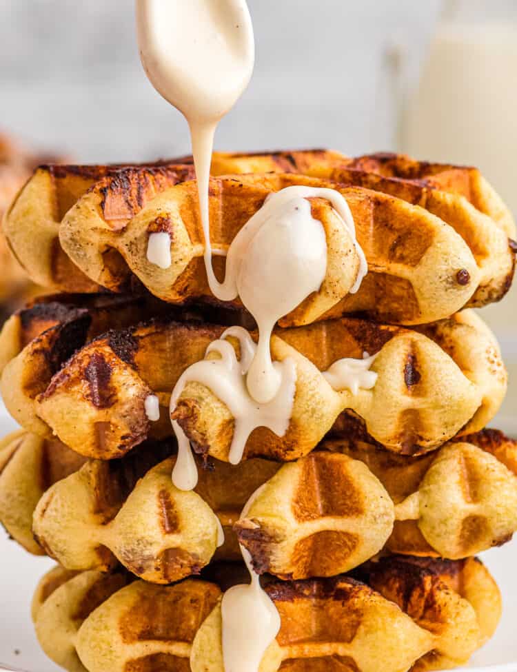 Cinnamon Roll Waffles stacked on plate with drizzle of frosting