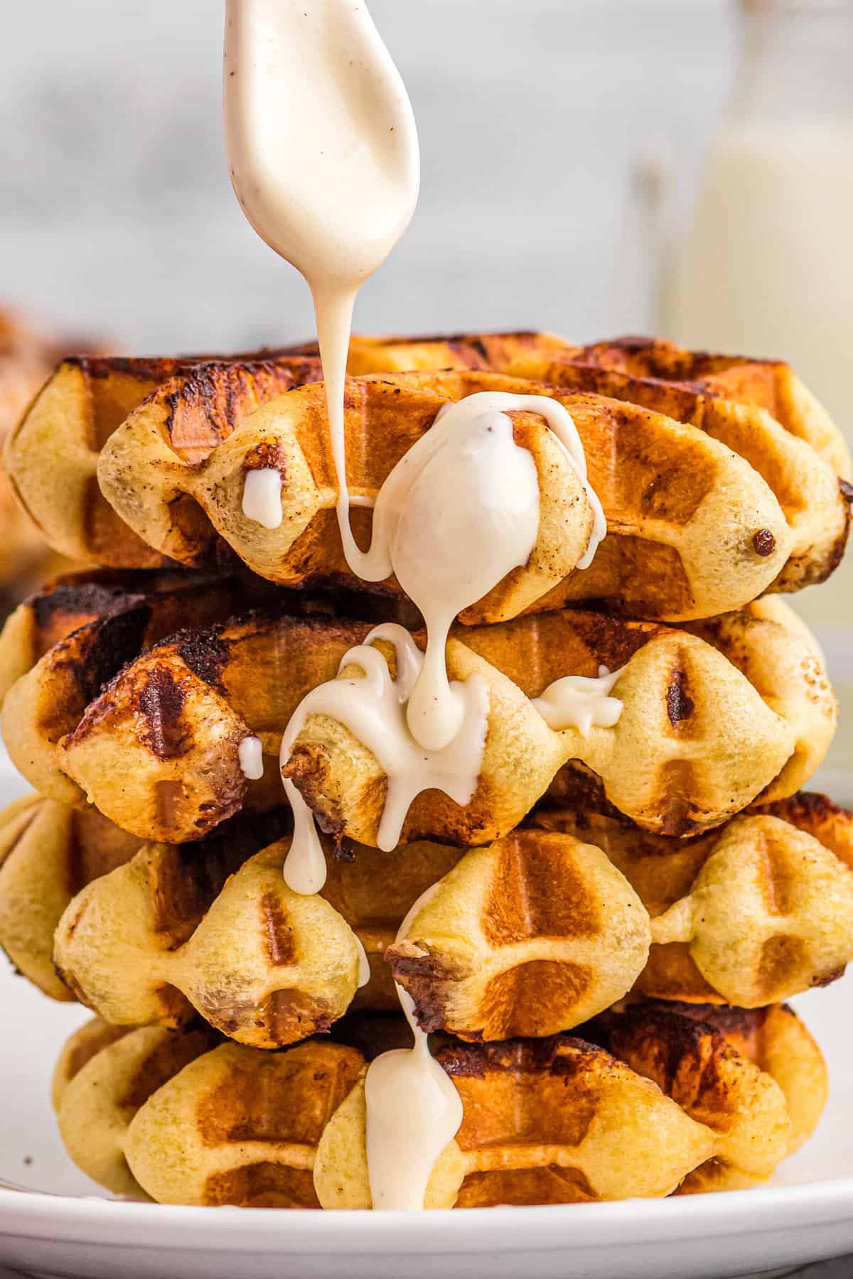 Cinnamon Roll Waffles stacked on plate with drizzle of frosting