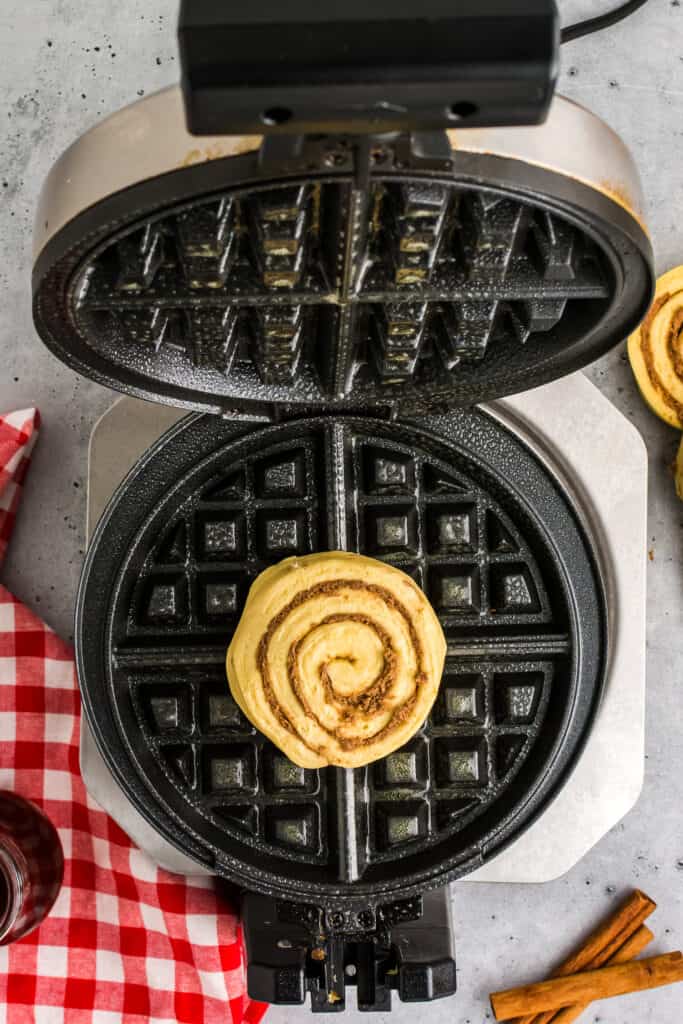 Heat up the waffle maker and add one slice of cinnamon roll to the waffle maker and bake.