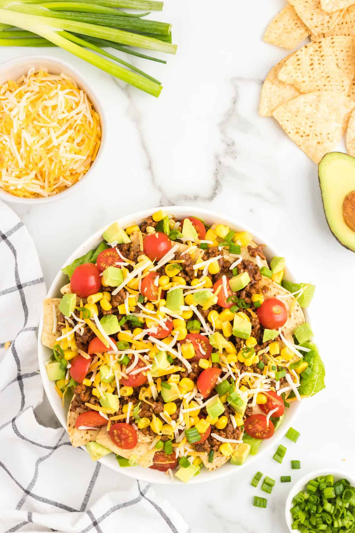 Topping taco salad with shredded cheese, corn, and diced avacados in bowl