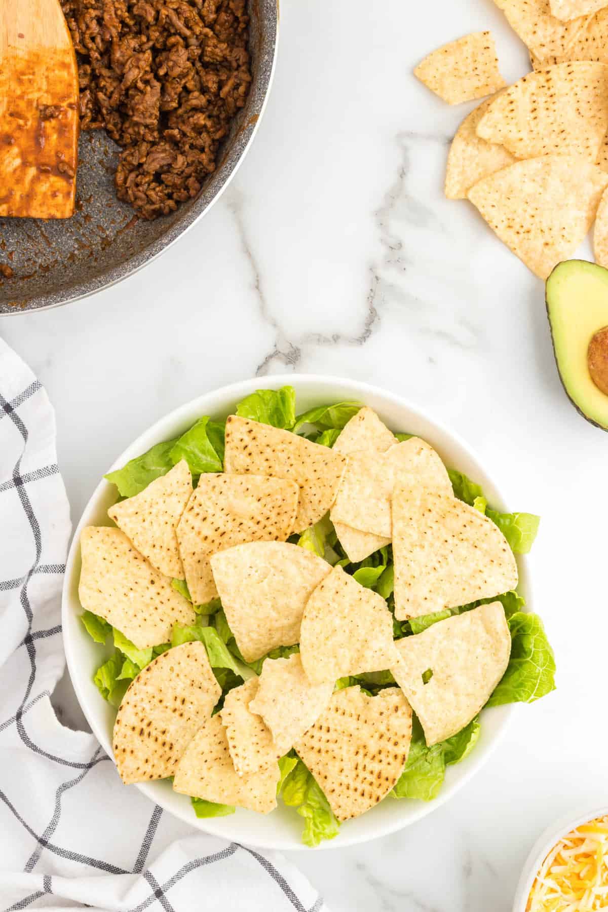 Topping lettuce with tortilla chips in bowl for taco salad
