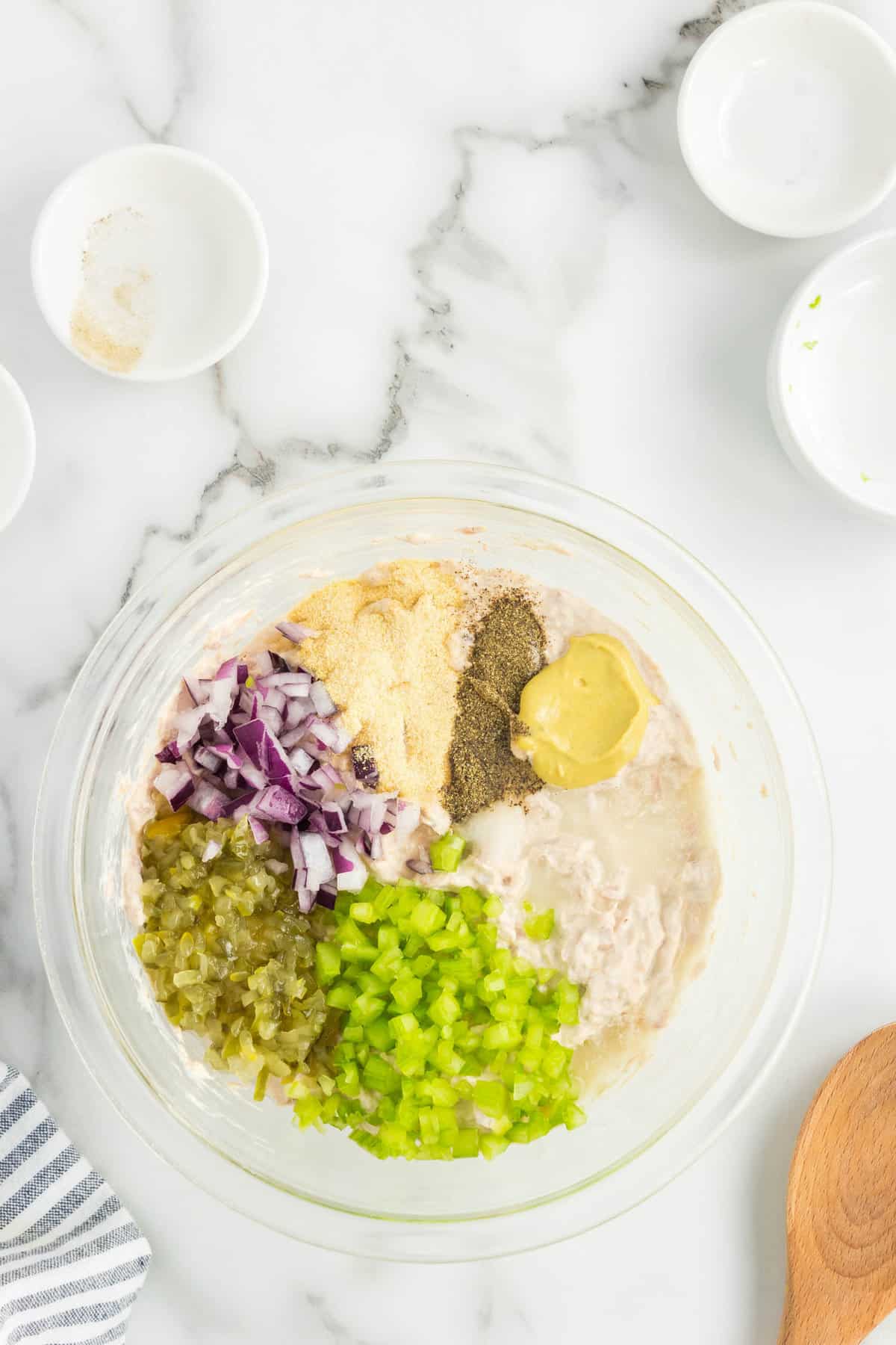 Adding seasonings and other ingredients to tuna and mayo mixture in bowl