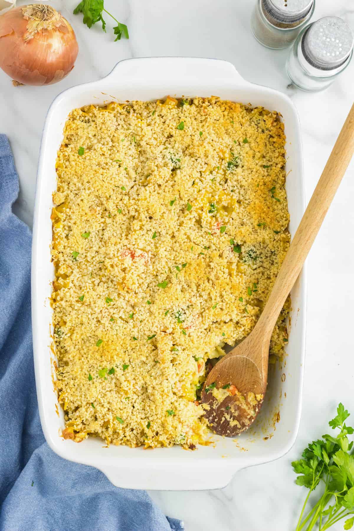 Using wooden spoon to scoop Chicken Noodle Casserole from 9x13 baking dish