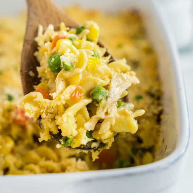 Scooping Chicken Noodle Casserole from Baking Dish with Wooden Spoon