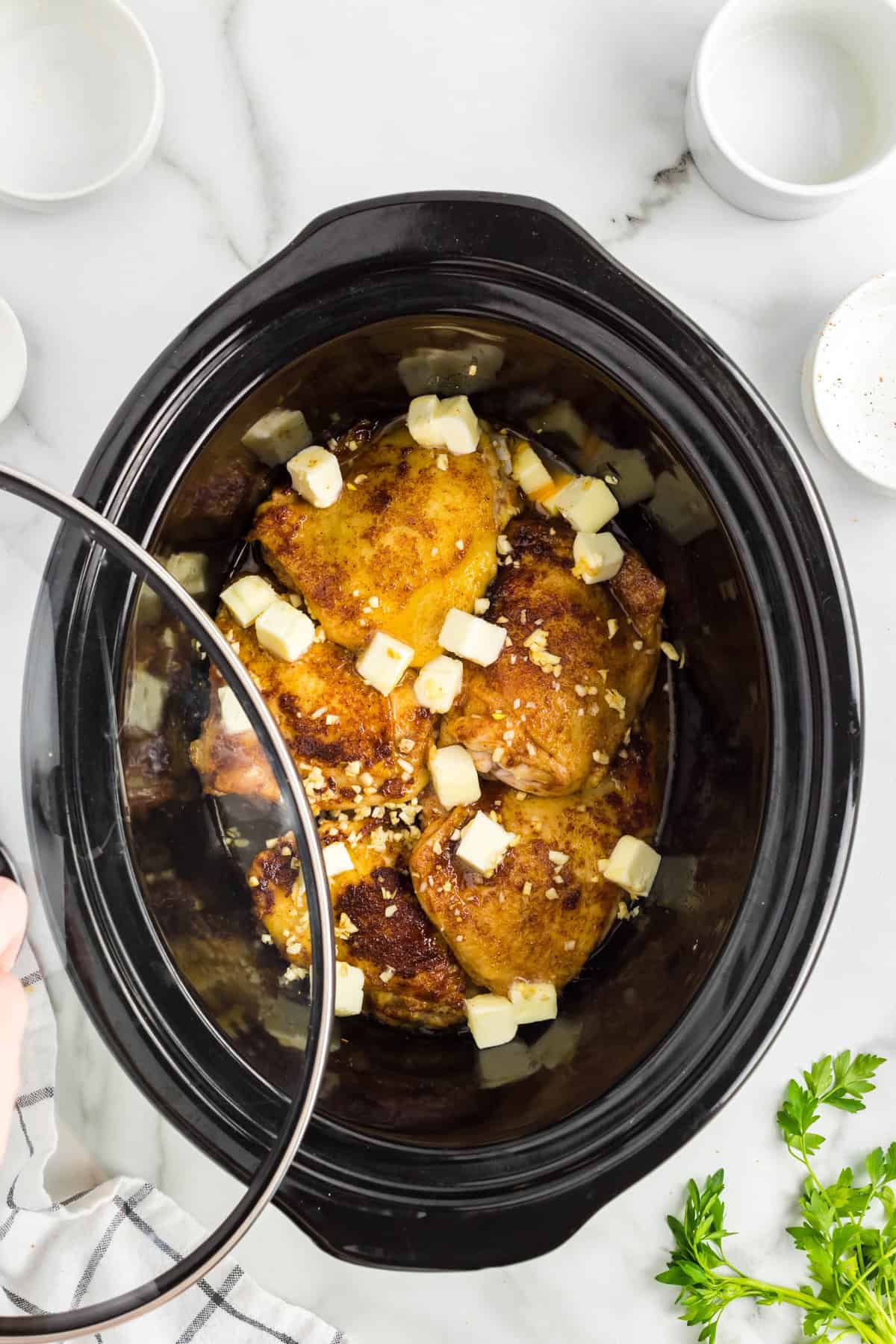 Adding cubed butter to thighs in crock pot and covering to simmer for Slow Cooker Chicken Thighs recipe