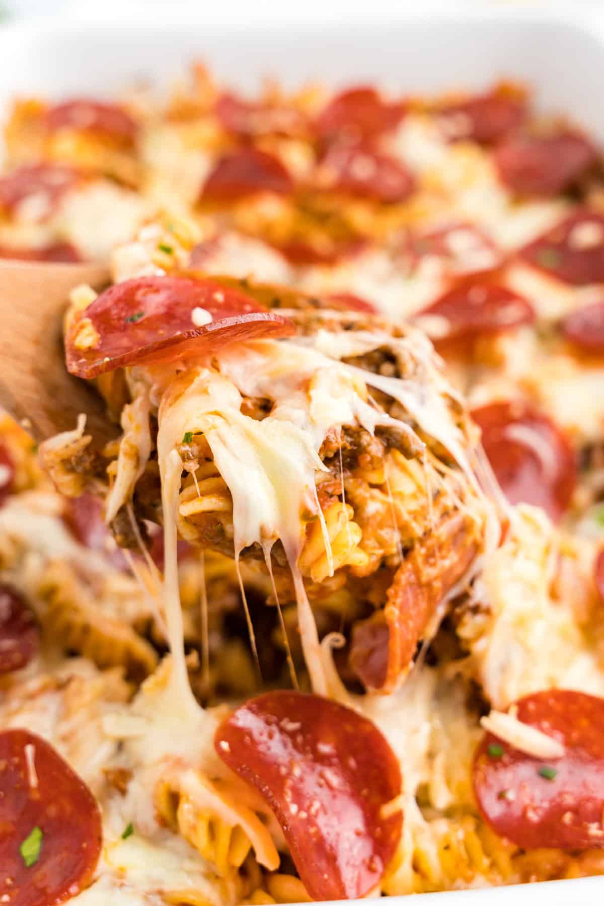 Pepperoni pizza casserole in baking dish with wooden spoon scooping out of the first bite