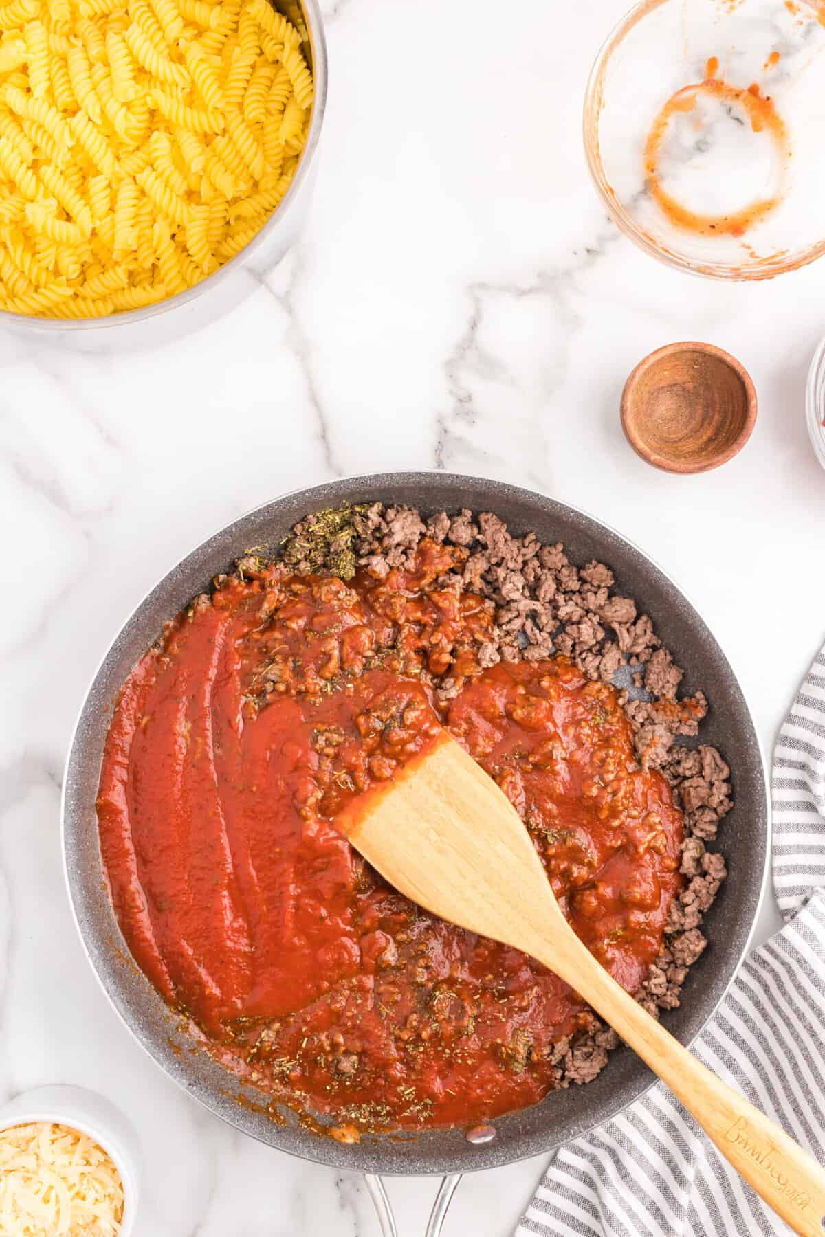 Stirring in sauce and seasoning to ground beef with wooden spoon in skillets for Pizza Casserole