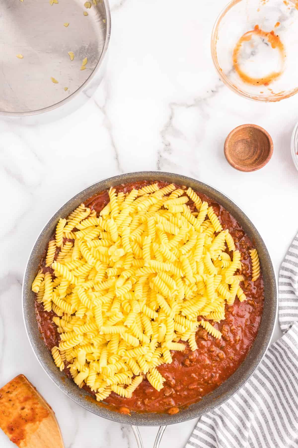 Adding uncooked spiral noddles to sauce and ground beef mixture for pepperoni pizza casserole