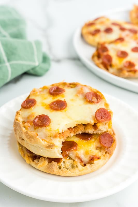 two English Muffin Pizzas on top of one another with one having a bite taken out of it.