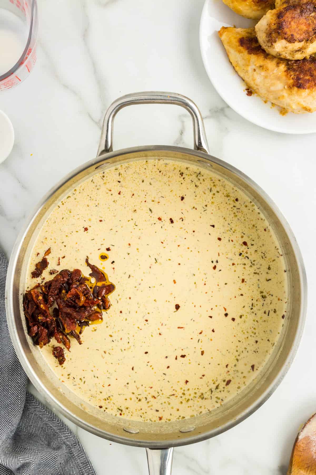 Adding sun-dried tomatoes into Marry Me Chicken sauce in pan