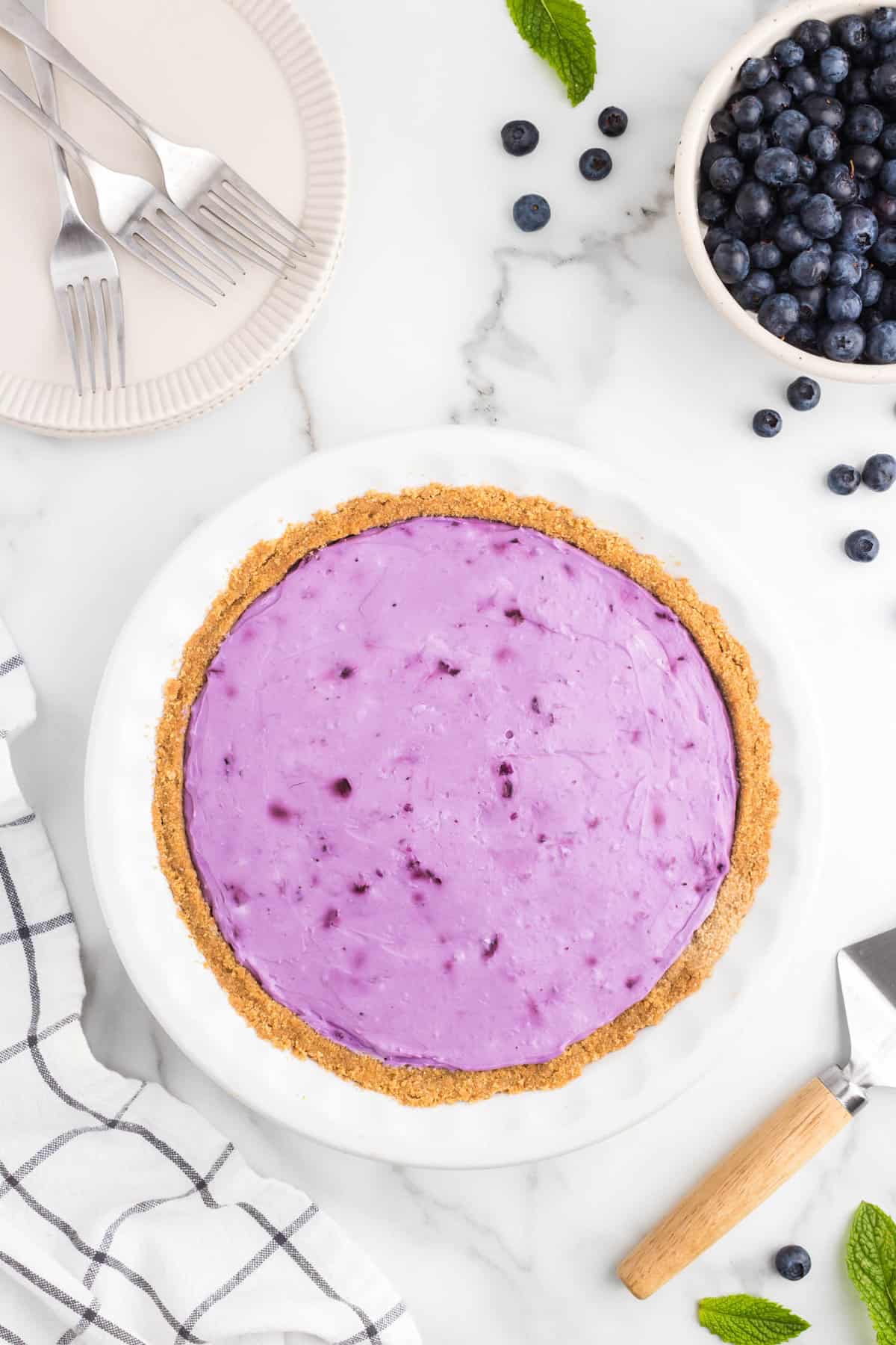 Spreading blueberry cheesecake mixture into prepared graham cracker crust for No Bake Blueberry Cheesecake recipe