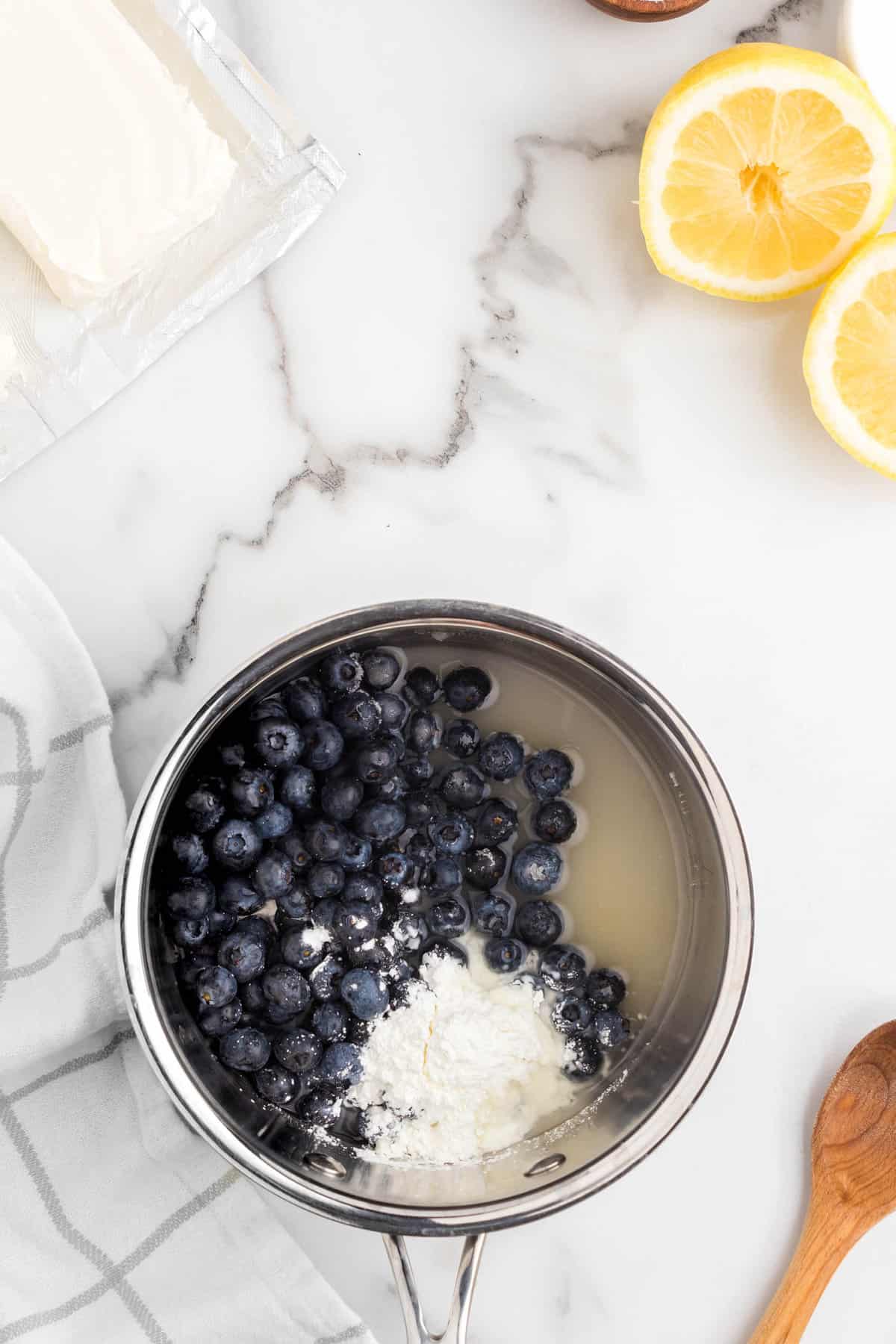 Adding blueberries, sugar, cornstarch, lemon juice and water to saucepan for No Bake Blueberry Cheesecake recipe