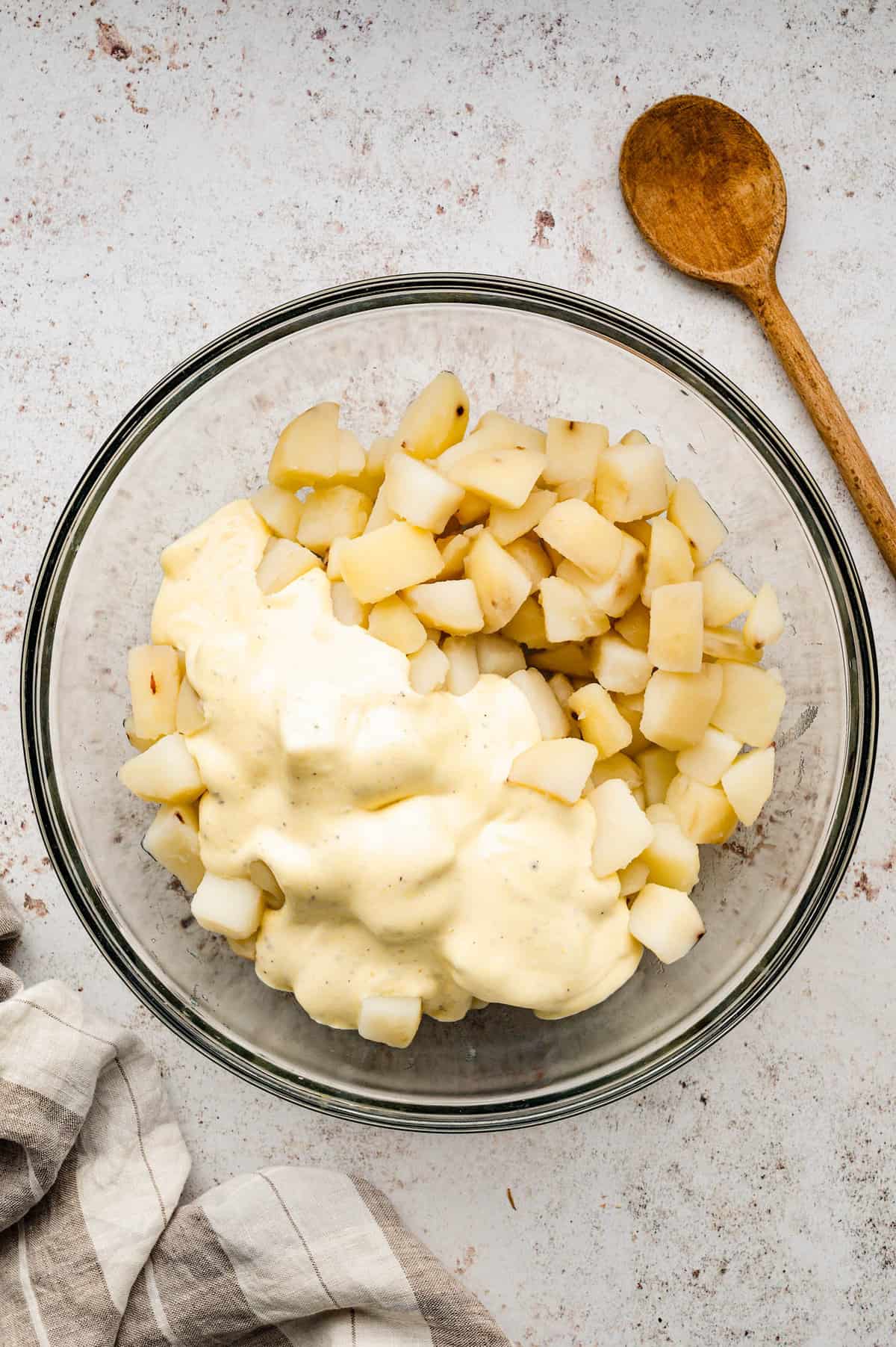 Adding dressing mixture to cooked diced potatoes in mixing bowl for homemade potato salad