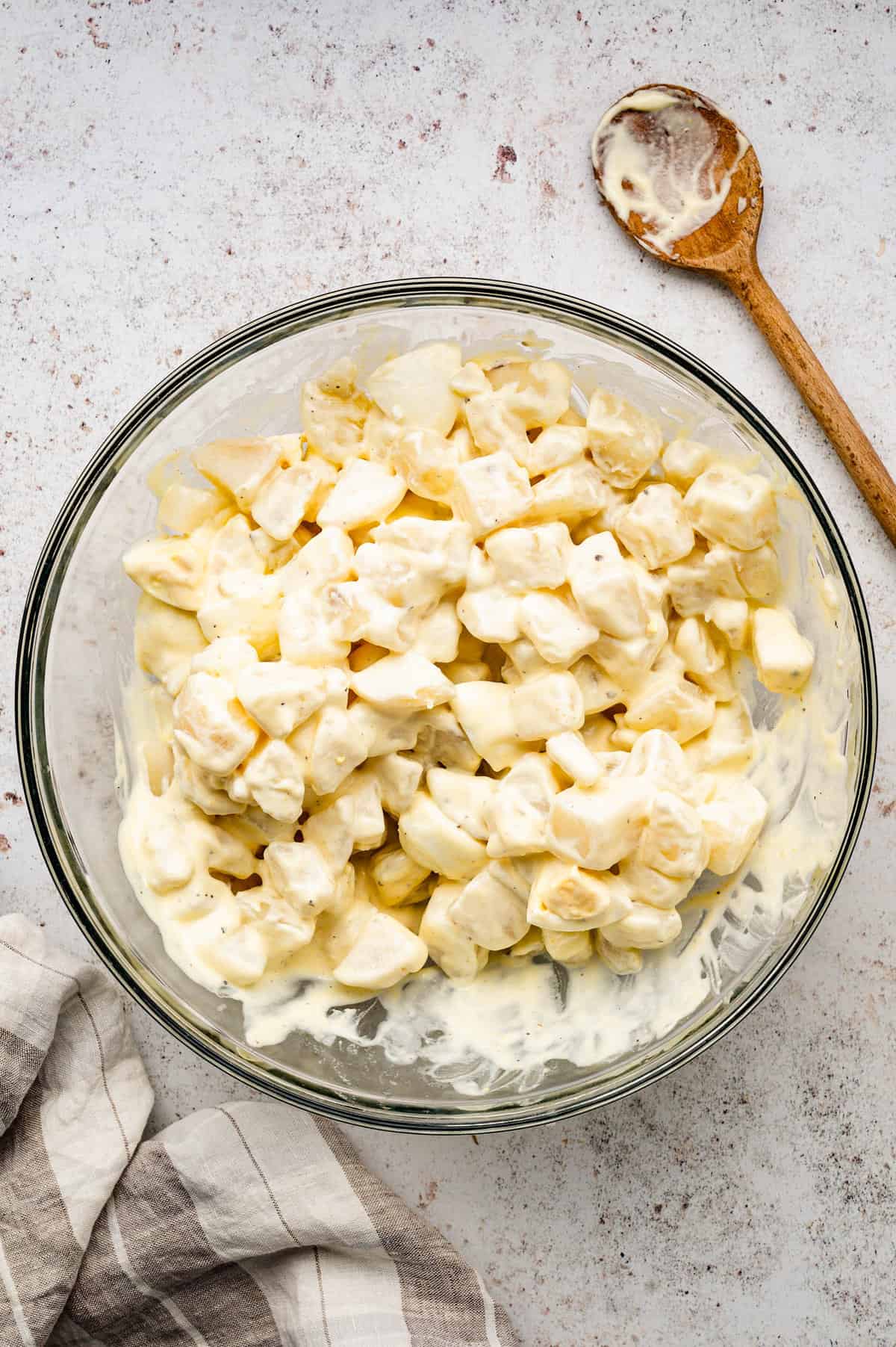 Combined potate salad ingredients in bowl with wooden spoon