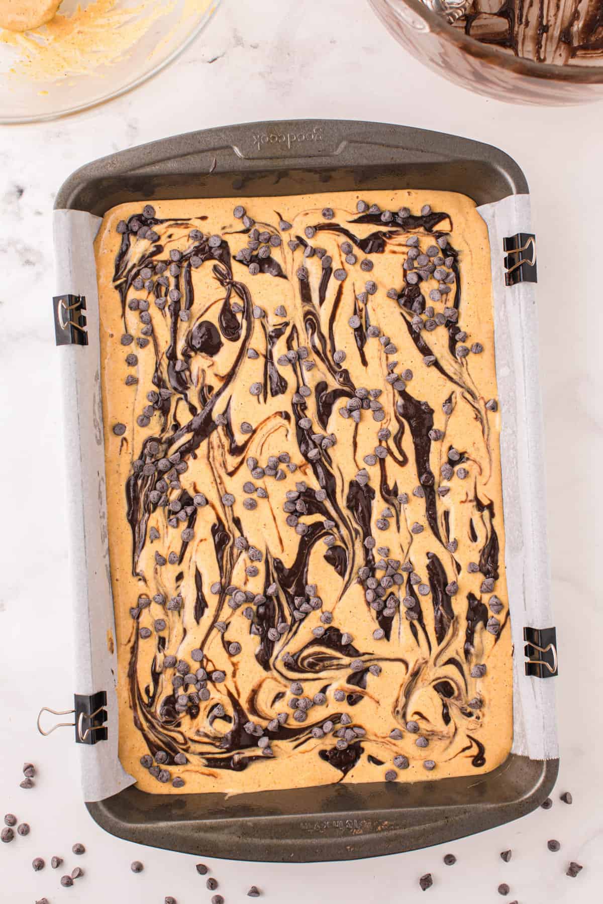 Swirling brownie mixture with mini chocolate chips on top of layers for Pumpkin Brownies Recipe