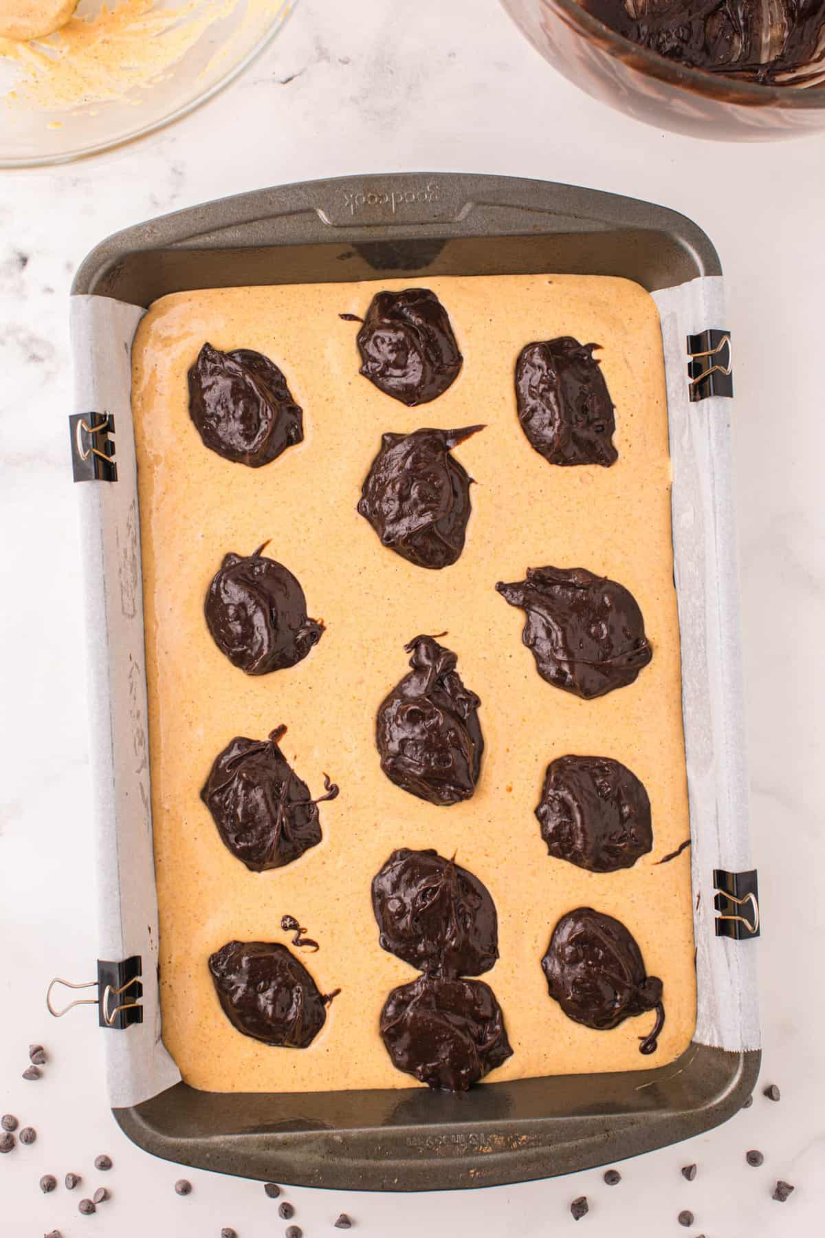 Adding spoonfuls of brownie mixture atop pumpkin layer in 9x13 baking pan for Pumpkin Brownies Recipe