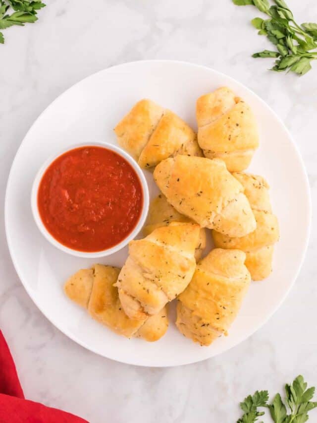 Crescent rolls displayed on a white plate with pizza sauce in a bowl.