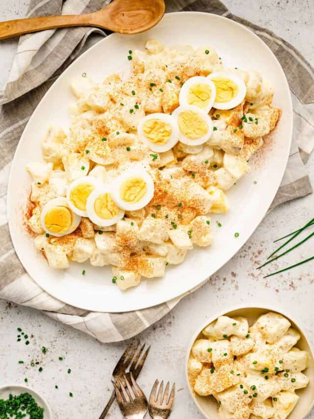 Bowl of potato salad topped with hard boiled egg slices and chives