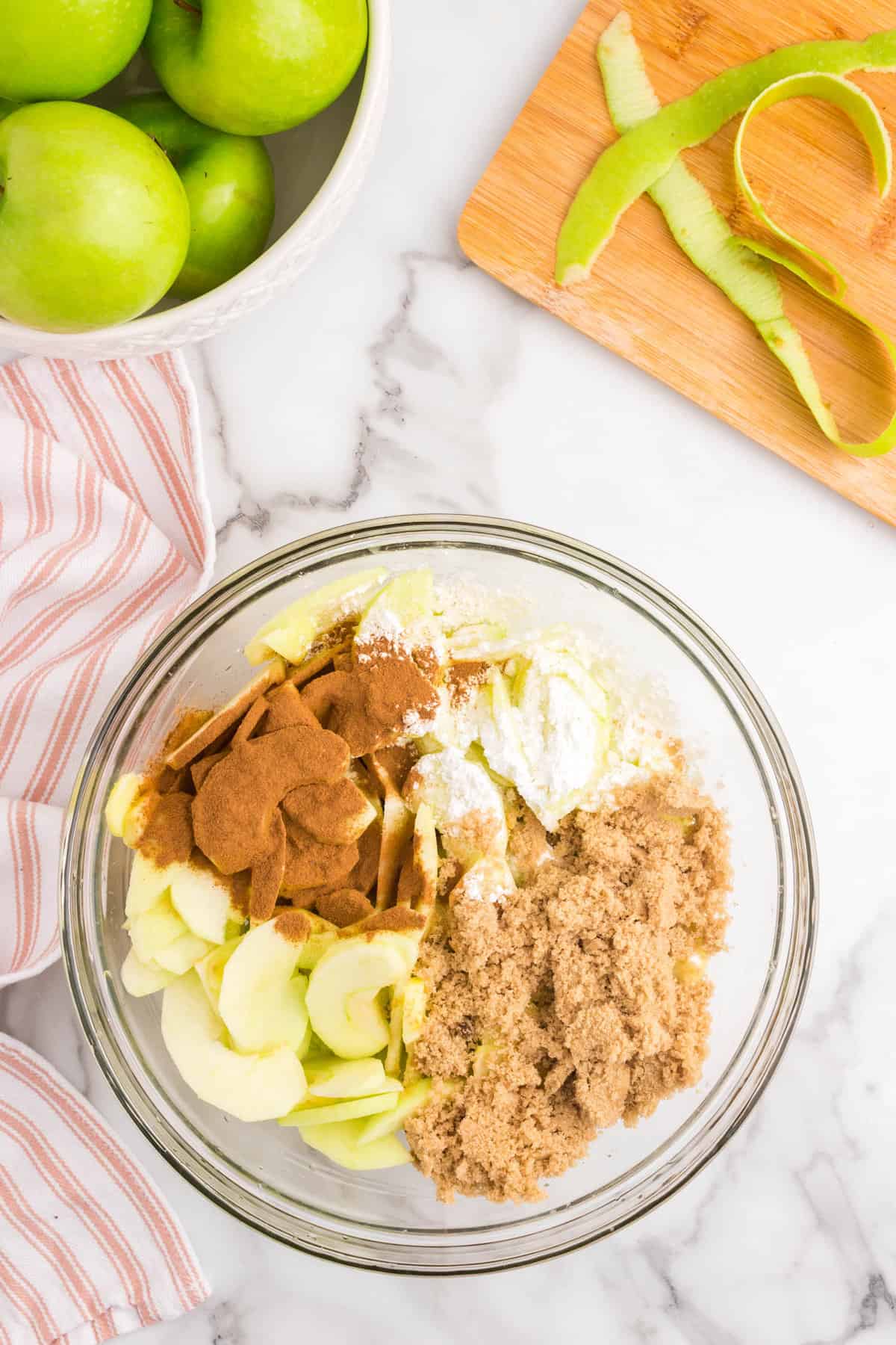 Tossing sliced granny smith apples in mixing bowl with spices for Apple Crumble recipe