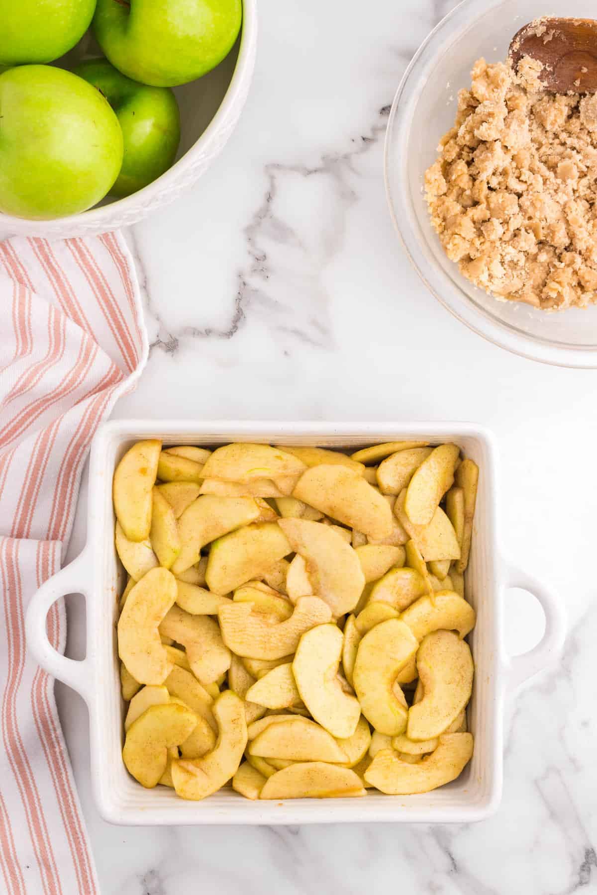 Filling tossed seasoned apples in square baking dish for Apple Crumble recipe