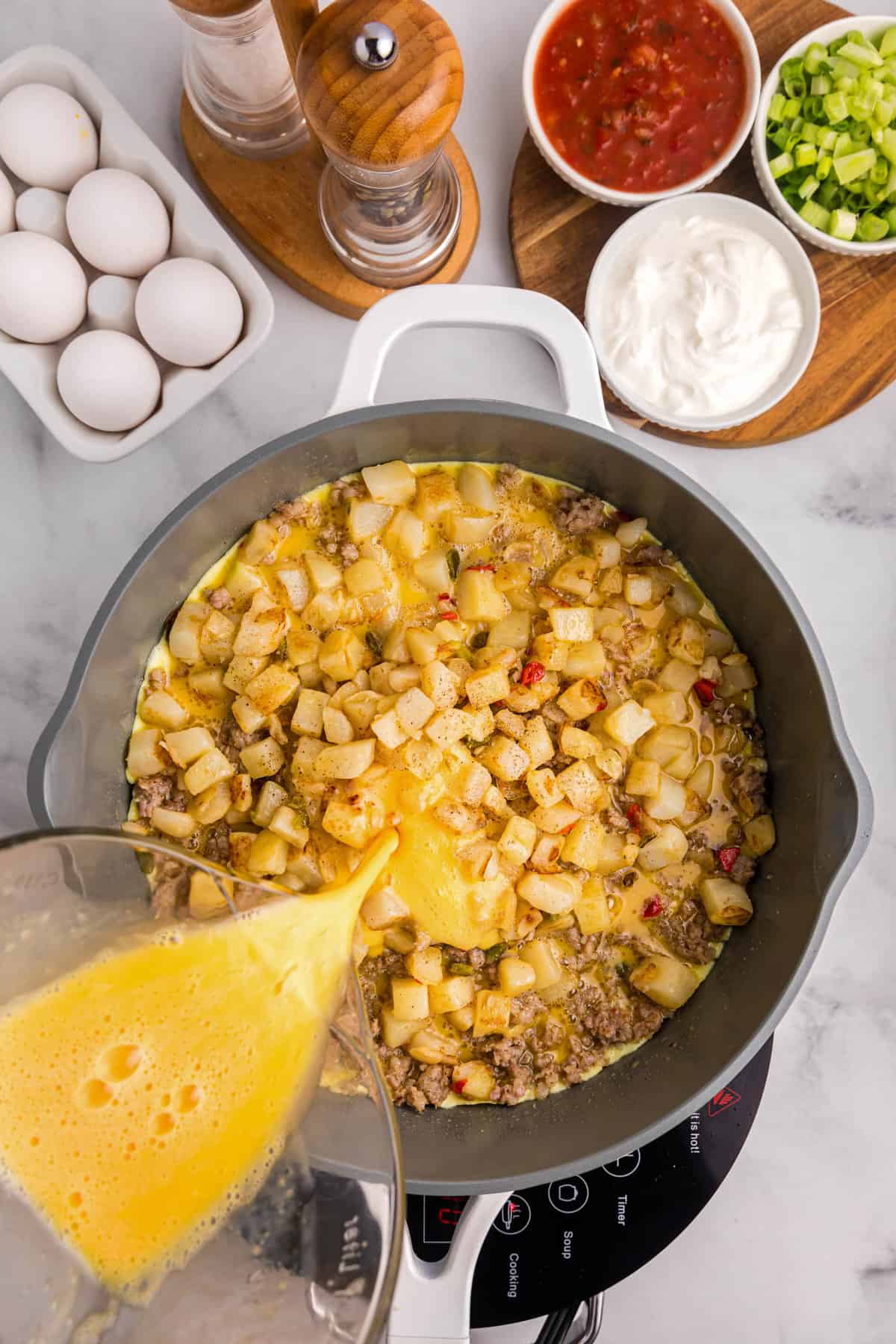 Pouring eggs into skillet with potatoes and sausage