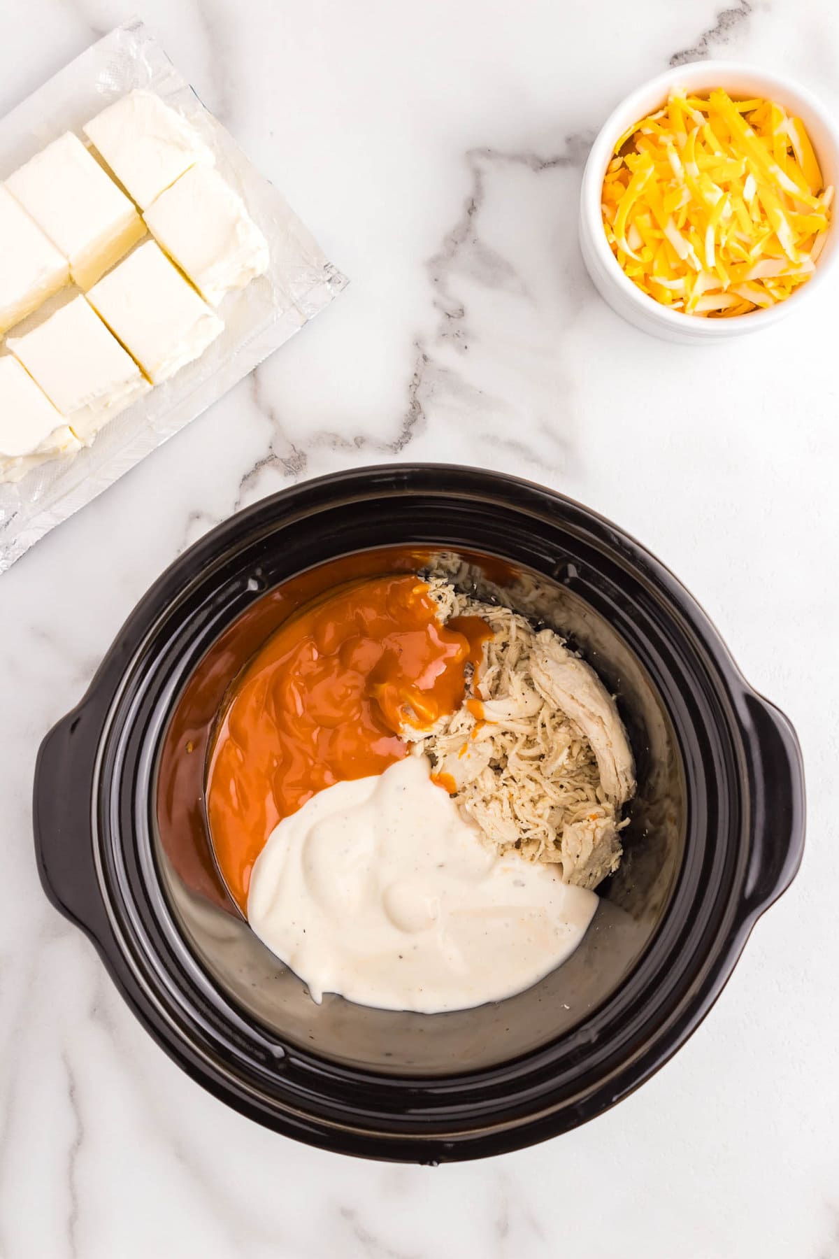 Shredded chicken, buffalo sauce, and ranch in crock pot for Buffalo Chicken Dip recipe