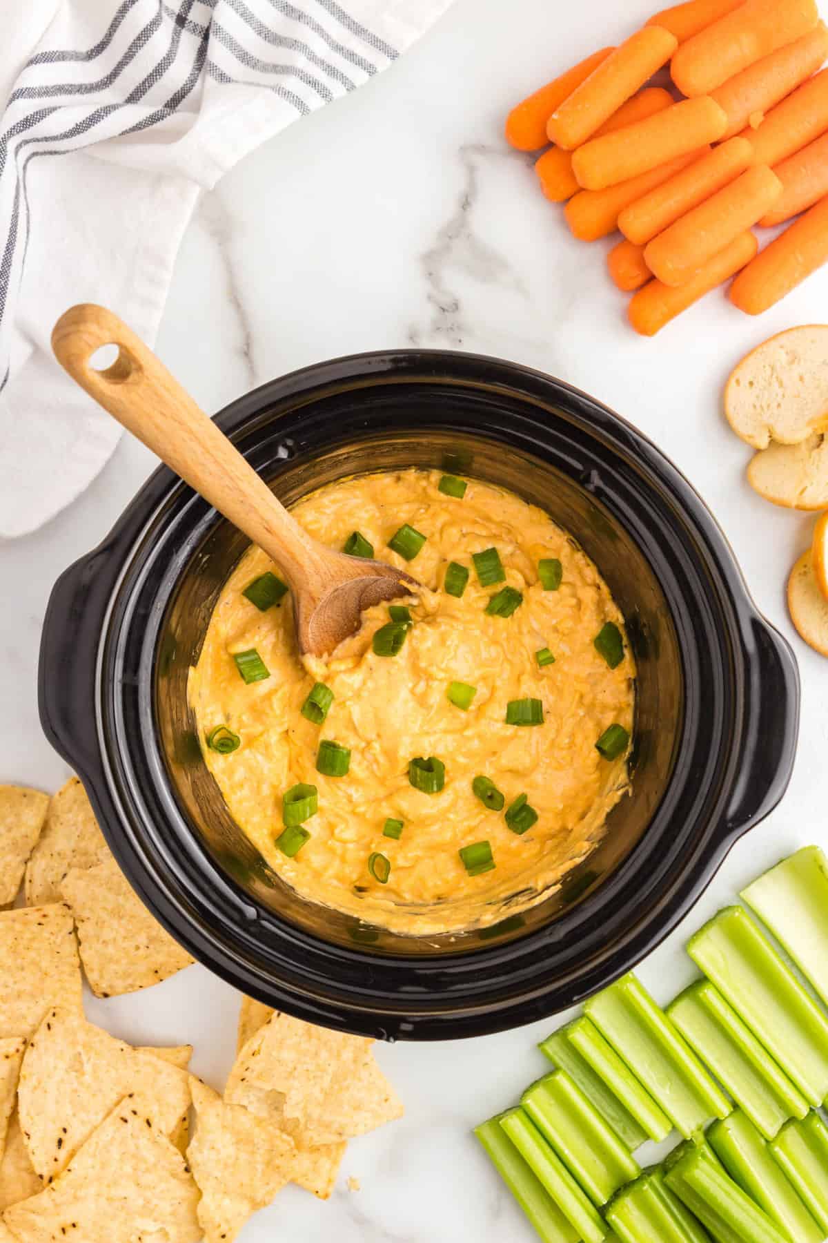 Buffalo Chicken Dip in crock pot garnished with chopped green onions with a variety of dippers