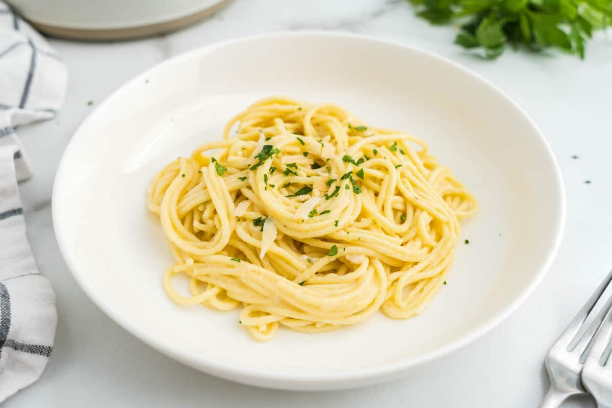 a White plate full of buttered noodles with fresh parsley on top.