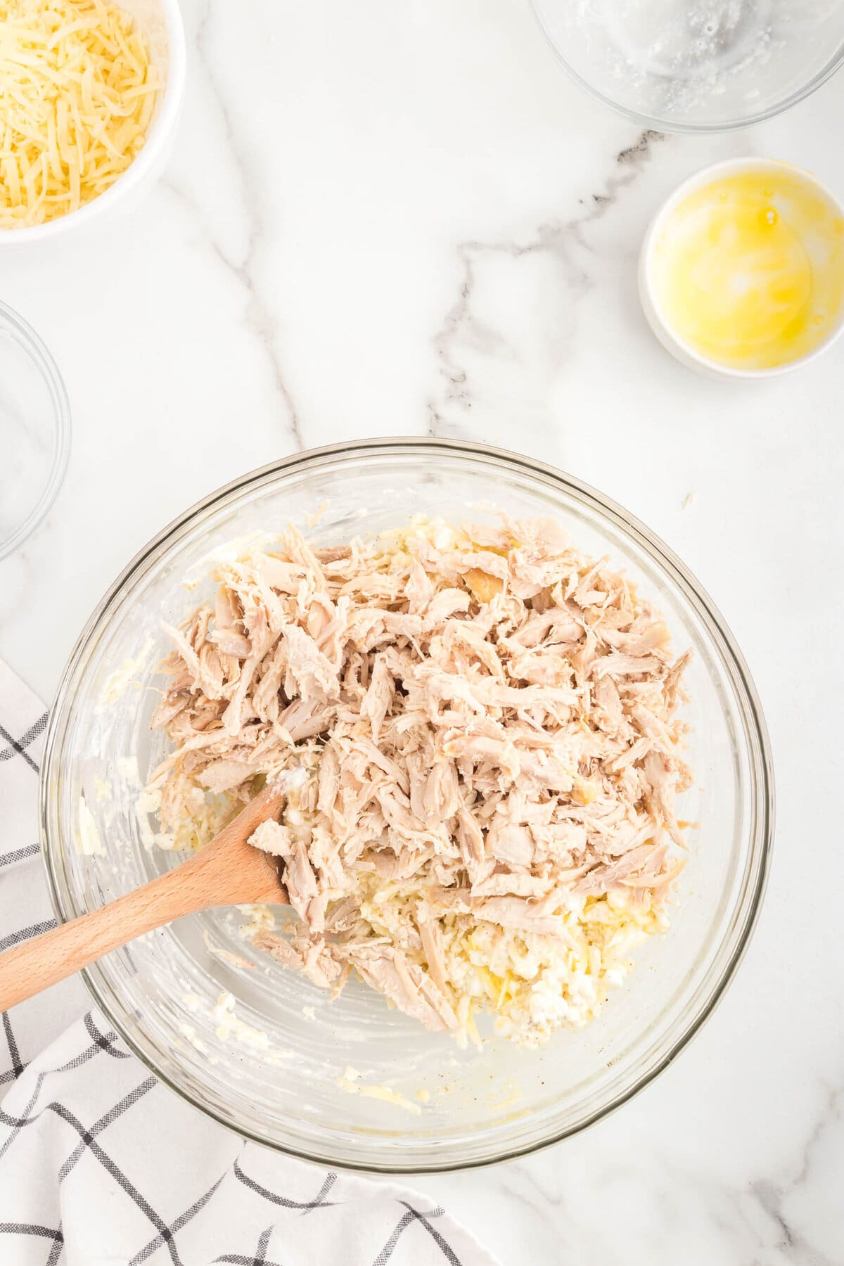 Adding cooked shredded chicken to cheese mixture for Mixing Chicken Alfredo Stuffed Shells cheeses in mixing bowl for Chicken Alfredo Stuffed Shells recipe