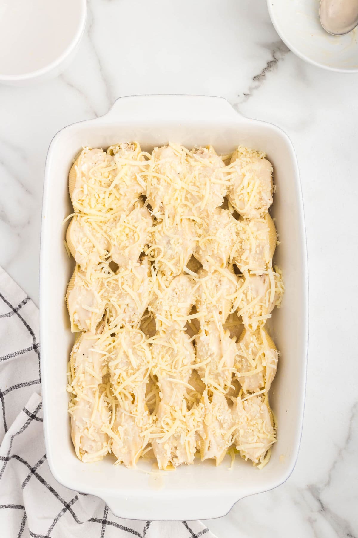 Topping stuffed shells with cheese in 9x13 baking dish for Alfredo Stuffed Shells