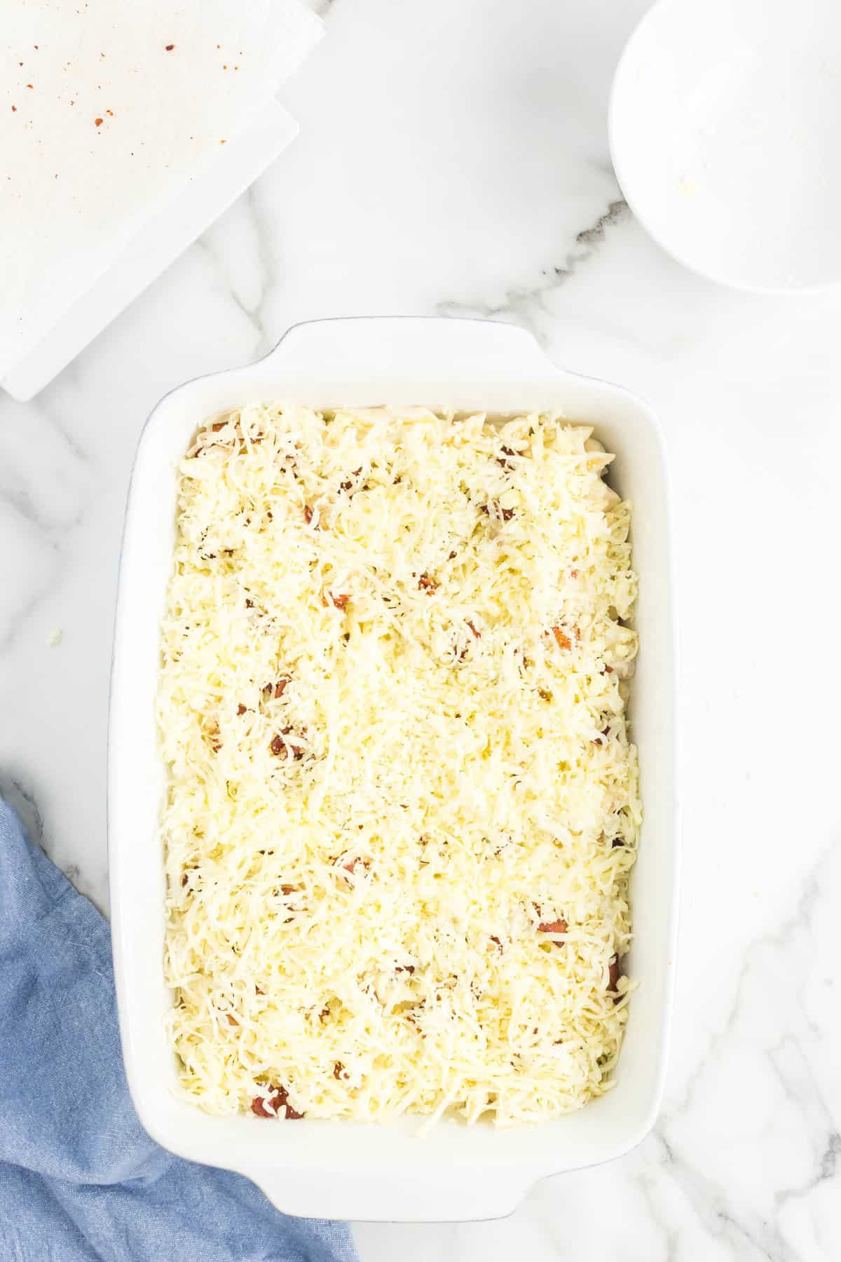 Topping casserole with shredded cheese for Chicken Bacon Ranch Pasta Bake
