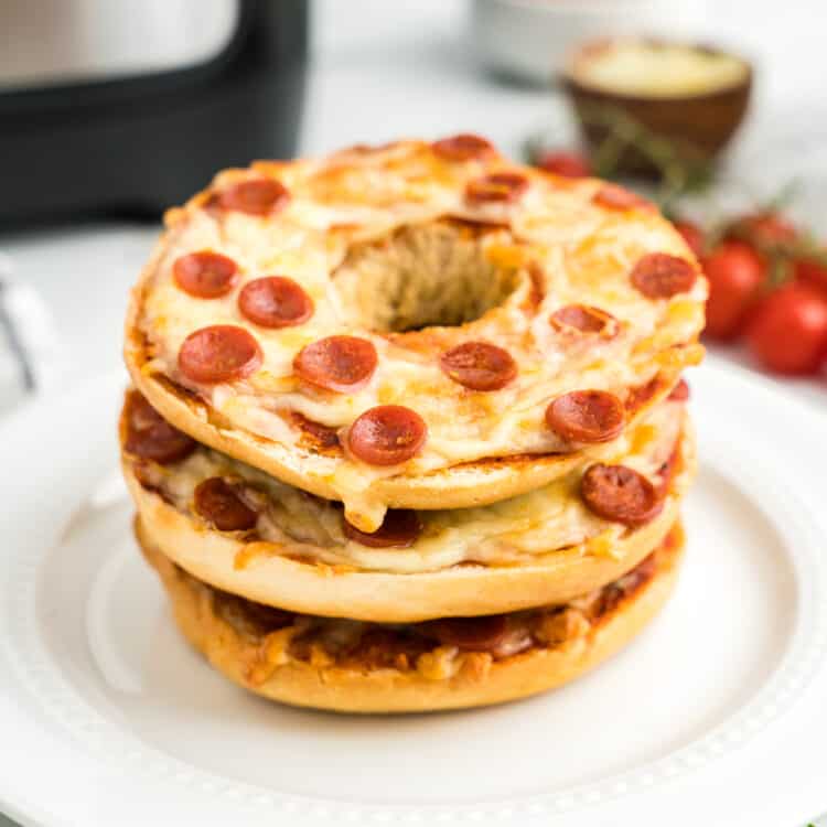 Pizza Bagels stacked on top of one another on a white plate.