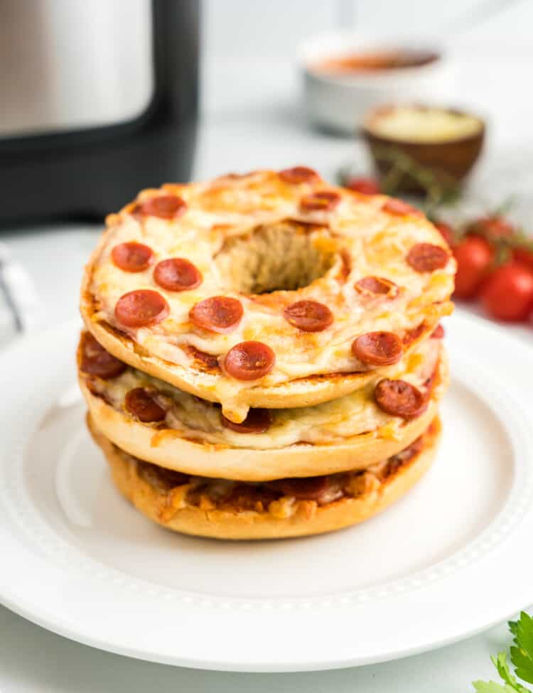 Pizza Bagels stacked on top of one another on a white plate.