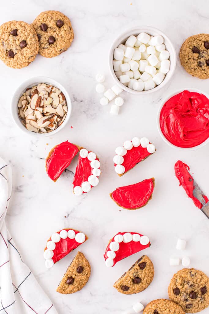 Cut each cookie in half and put red frosting on the flat or bottom side of the cookie.Place mini marshmallows around the curved edge of the cookie.