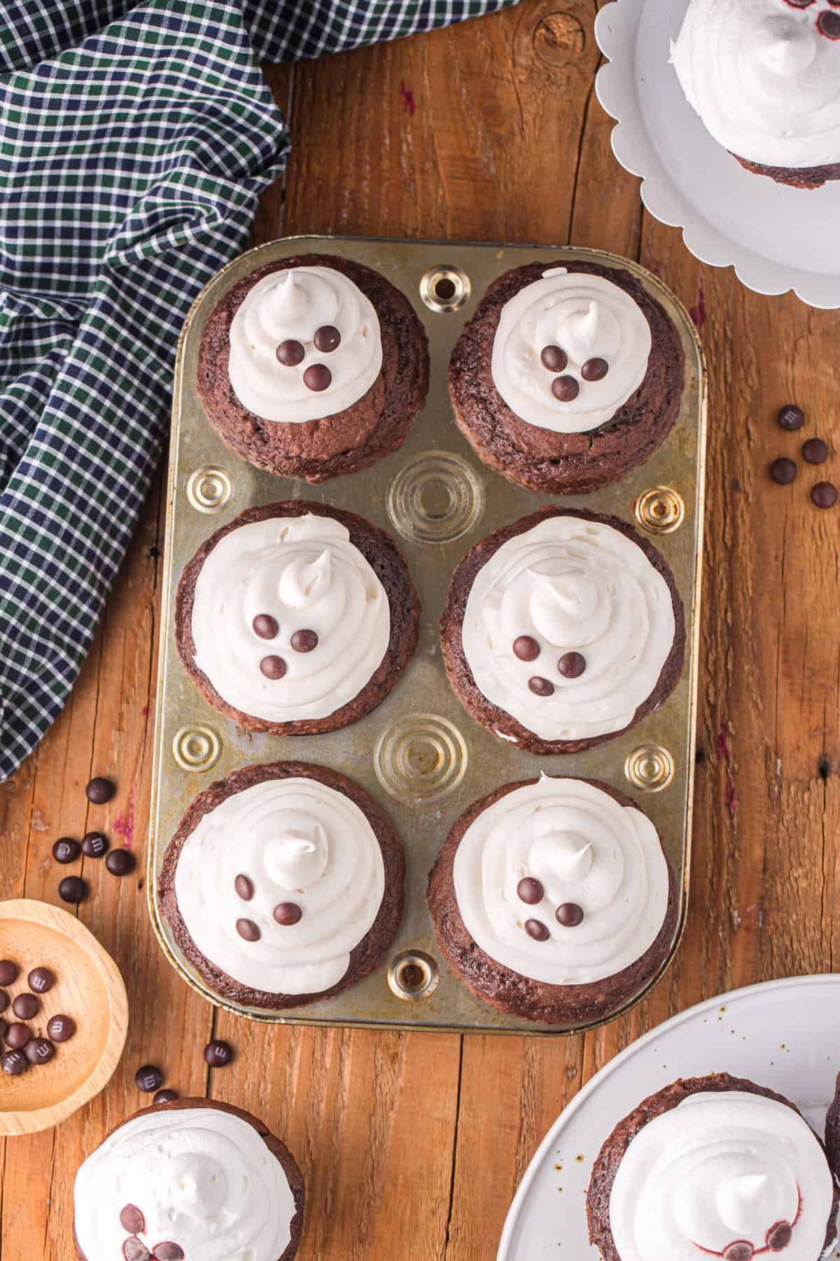 For the frosting, place a half of a marshmallow on top of the cupcake and put the frosting into a piping bag. Pipe frosting around the bottom of the marshmallow and work your way up to make it look like an ice cream type spiral and add three M&Ms for the face.