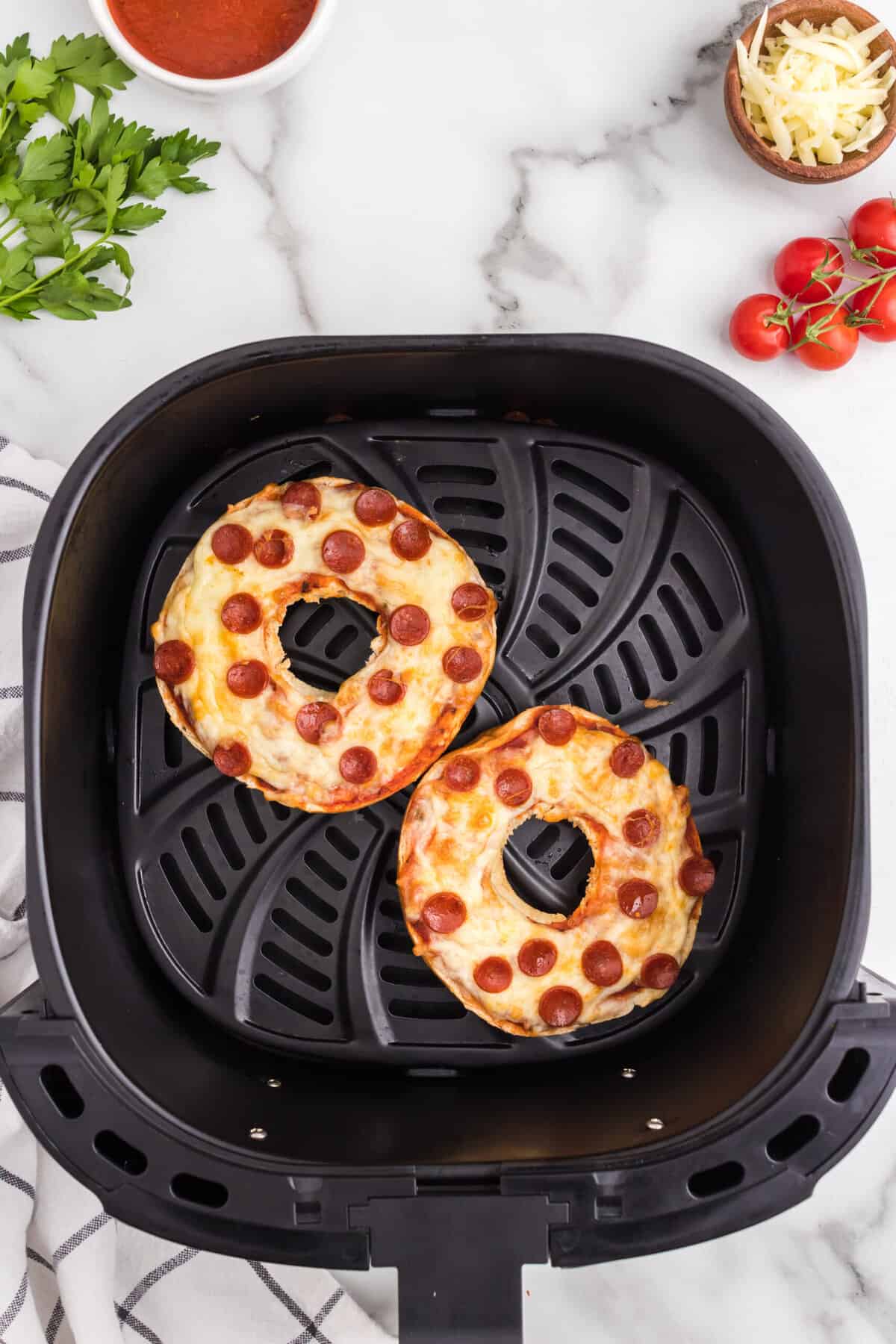 Pizza Bagels Cooked sitting in an Air Fryer Basket.