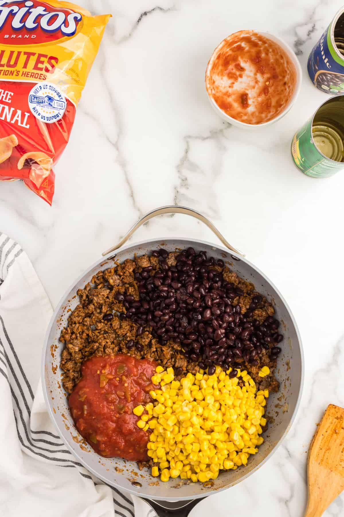 Adding corn, salsa, and black beans to seasoned ground beef in skillet for Frito Pie Casserole