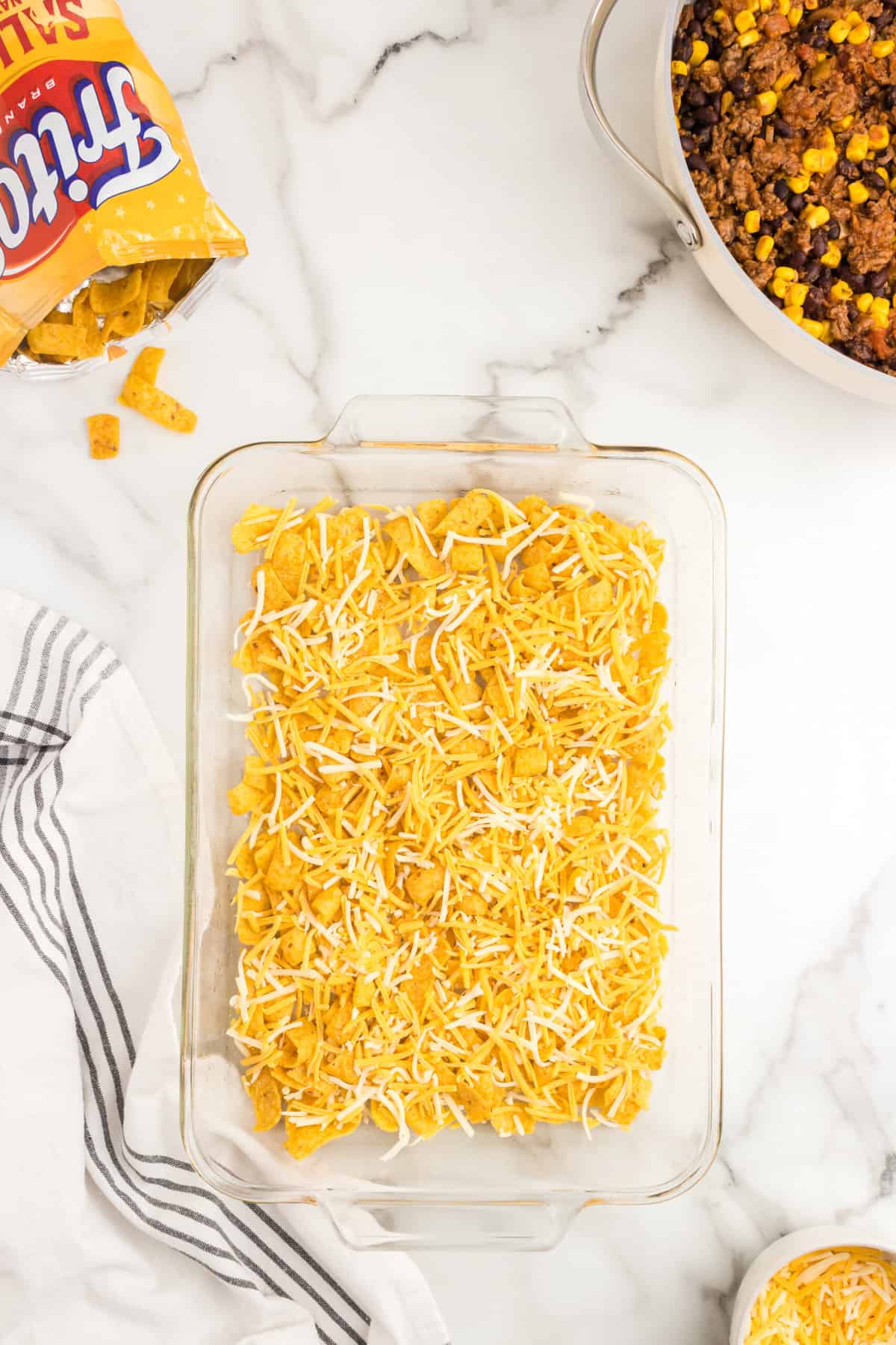 Topping Fritos layer with shredded cheese for Frito Pie Casserole