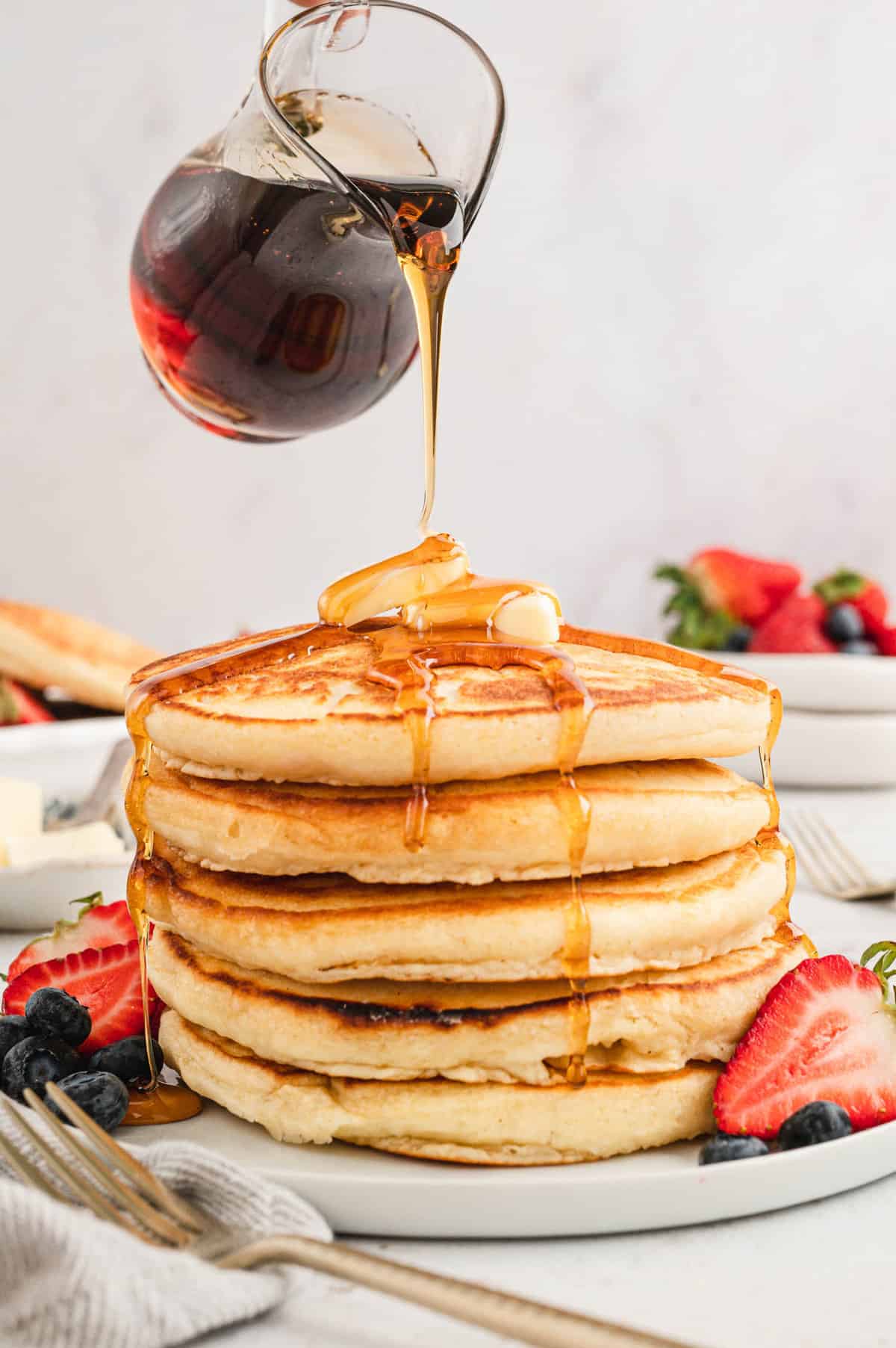 Homemade Pancakes stacked on plate with butter, syrup, and fresh fruit