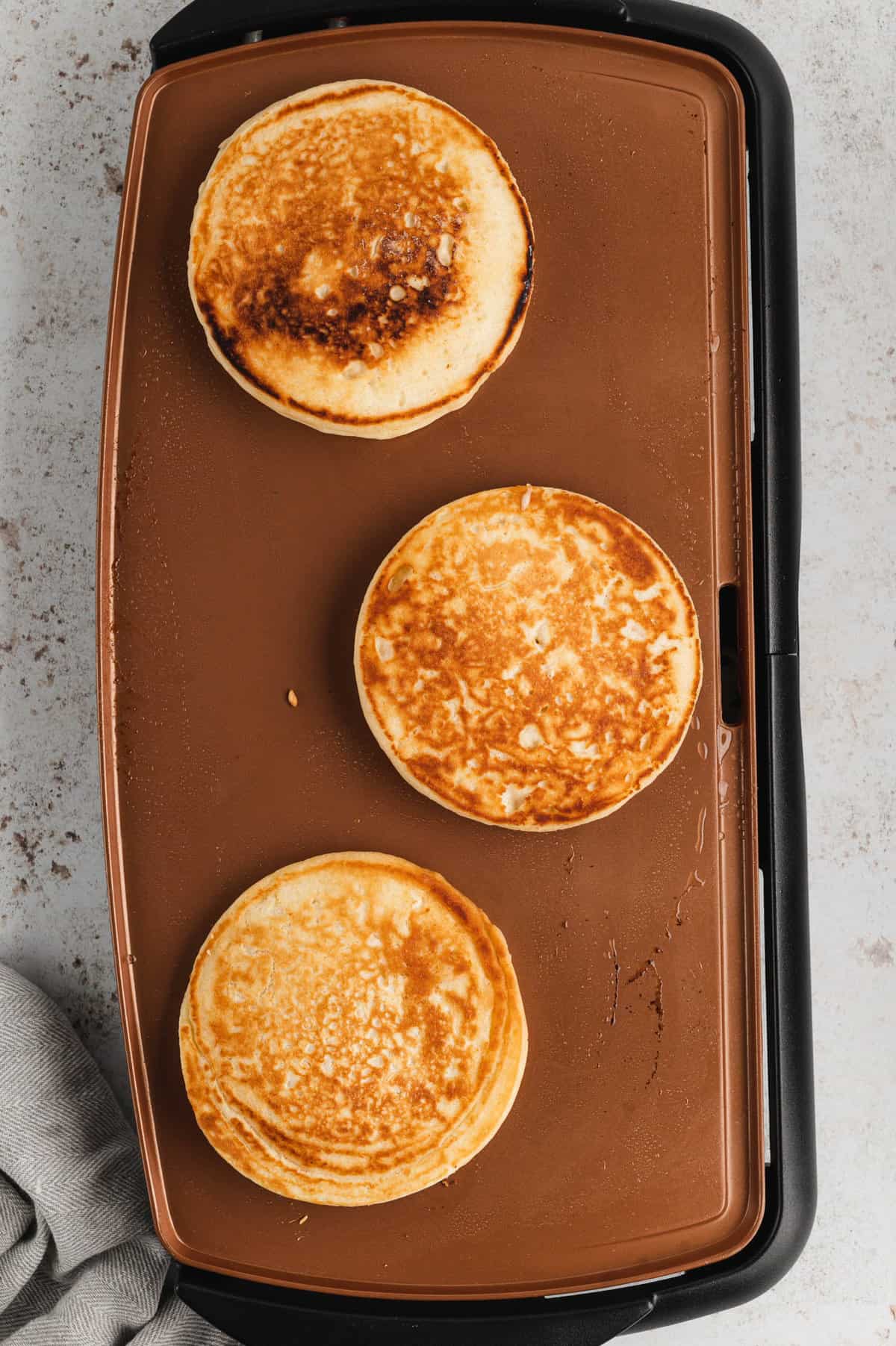 Golden brown pancakes on greased griddle for Homemade Pancakes Recipe