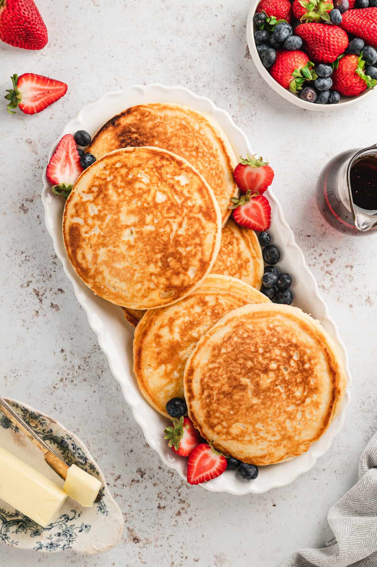 Golden brown homemade pancakes on serving tray with fresh fruit
