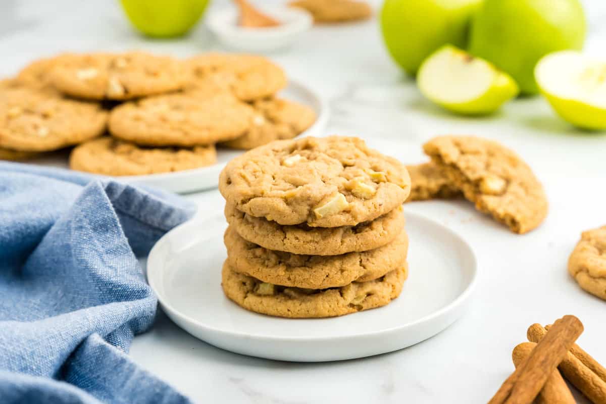 Apple and Peanut Butter Cookies stacked on plate with apples and cinnamon in background